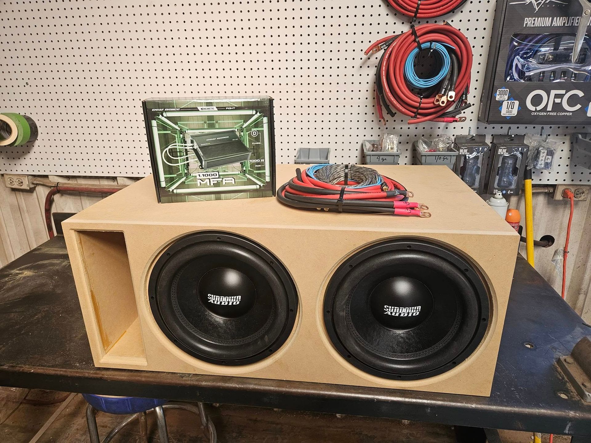 DIY cardboard speaker box with two black subwoofers on a workbench in a garage-like shop.