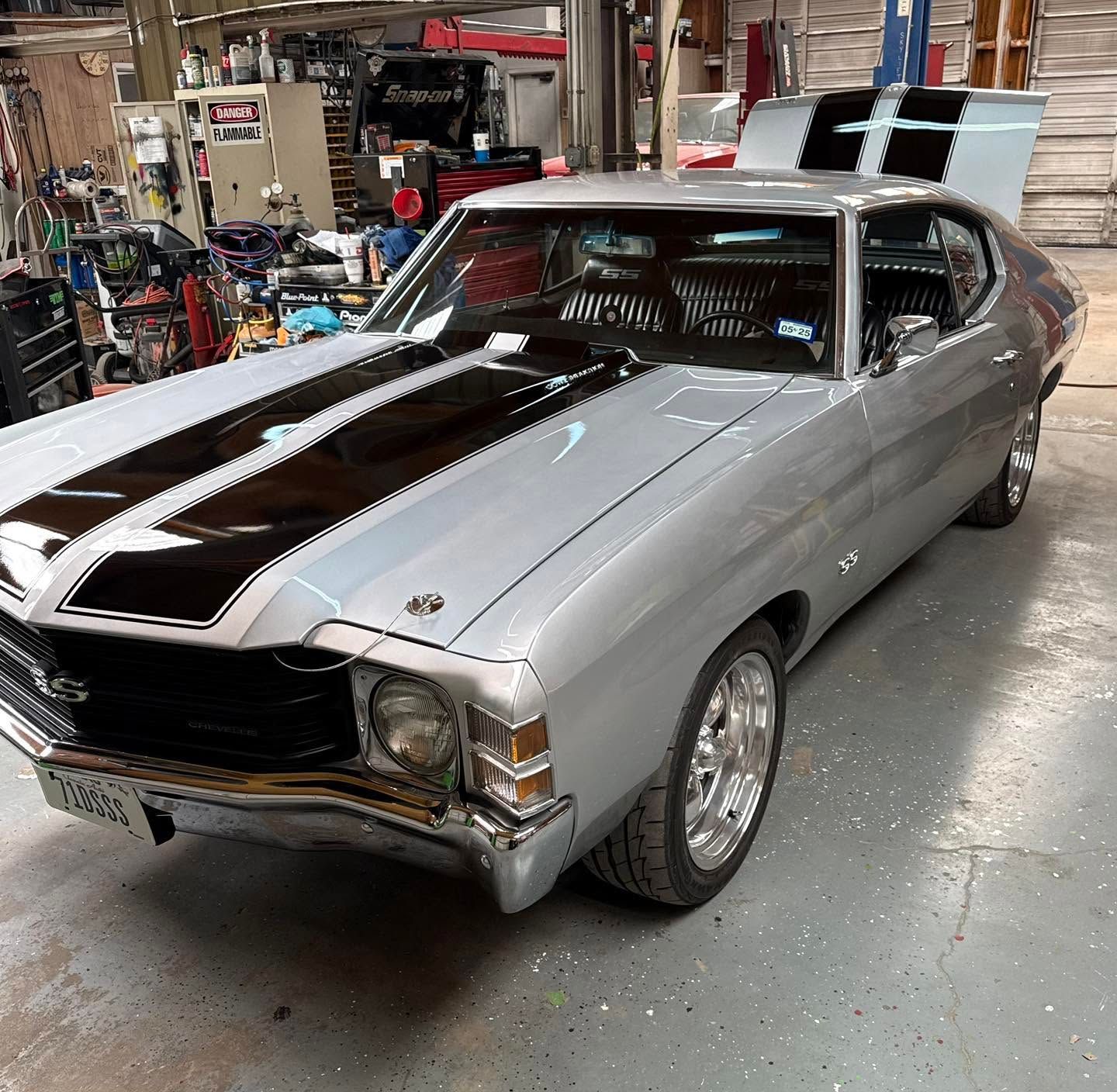 Silver classic muscle car with black racing stripes parked in a garage