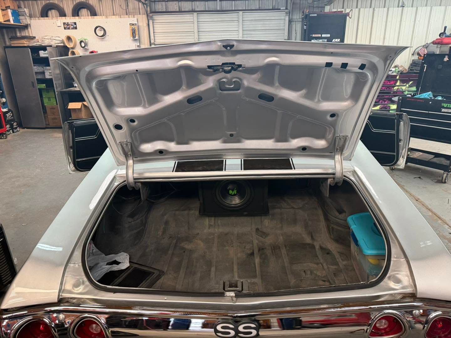 Open car trunk with hood raised in an auto shop, showing the empty cargo area.