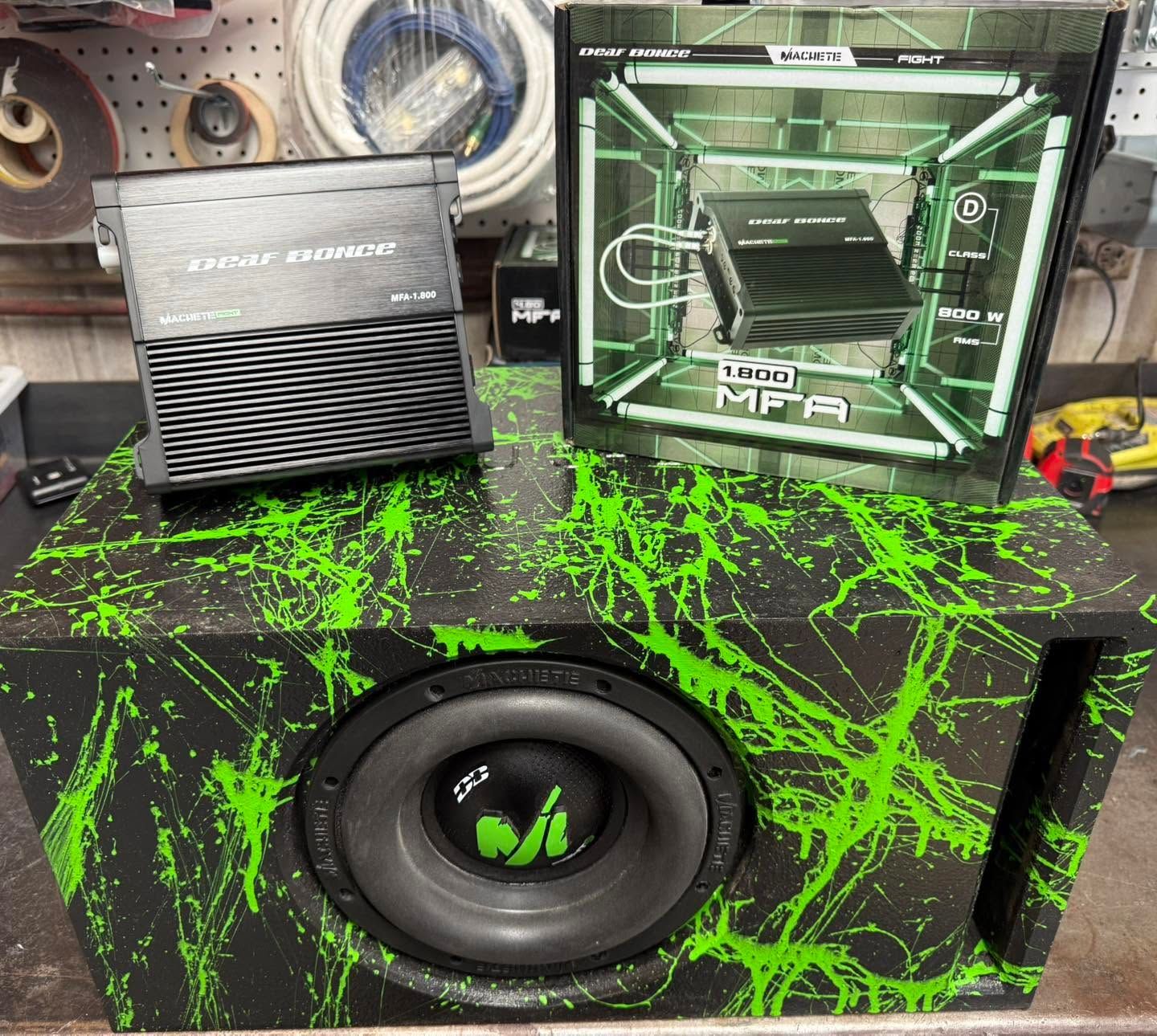 Custom car audio setup with green splatter-pattern subwoofer box and amplifier on a display table