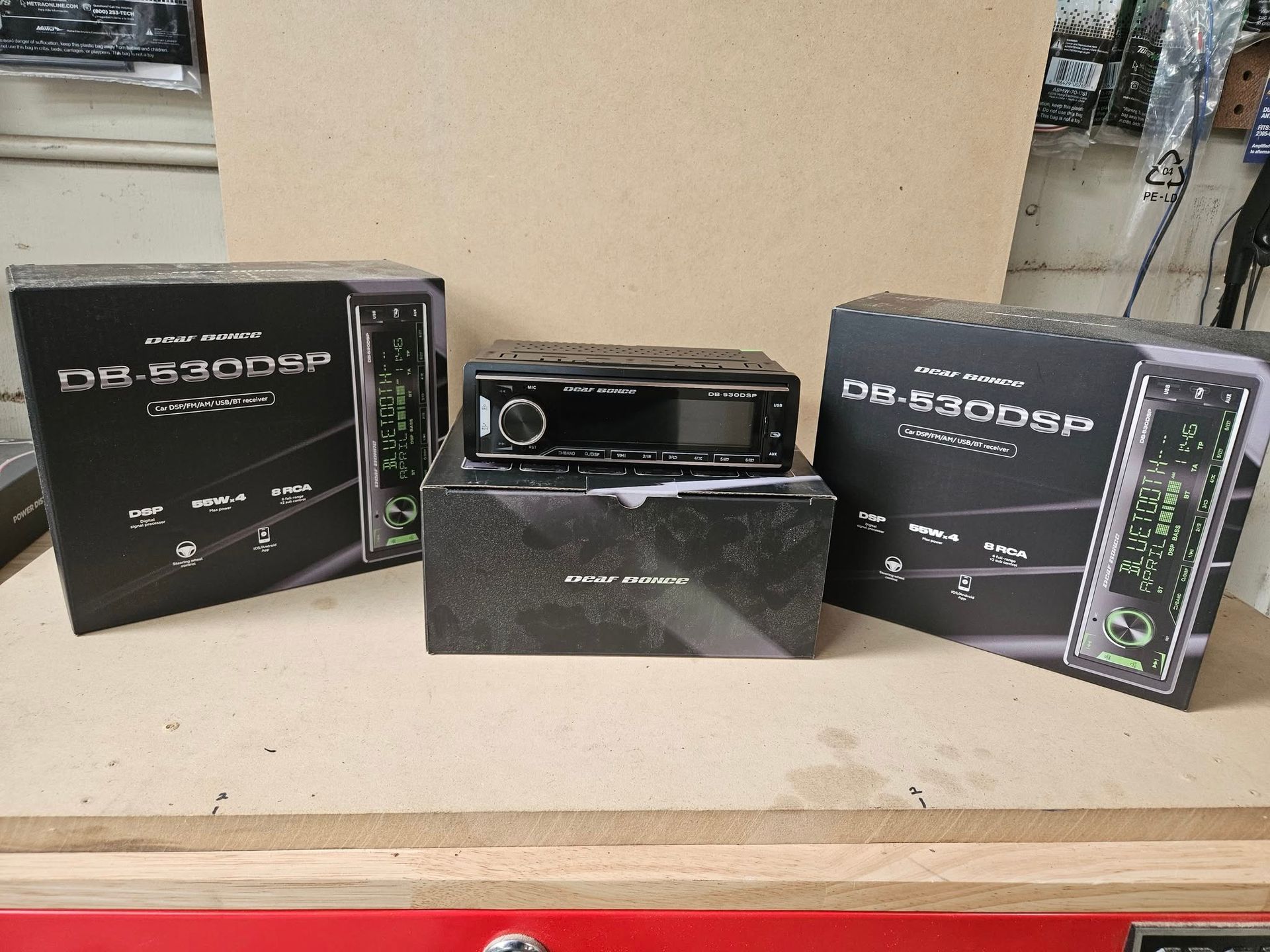 Three black audio components and boxes displayed on a beige shelf with a potted plant behind them