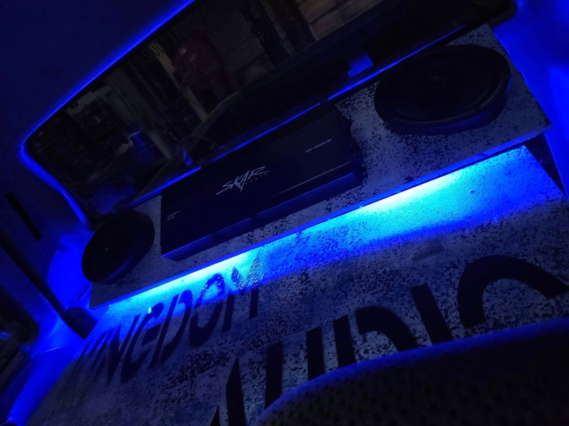 Blue-lit ceiling with a shelf, speakers, and a neon sign reading “DARK.”