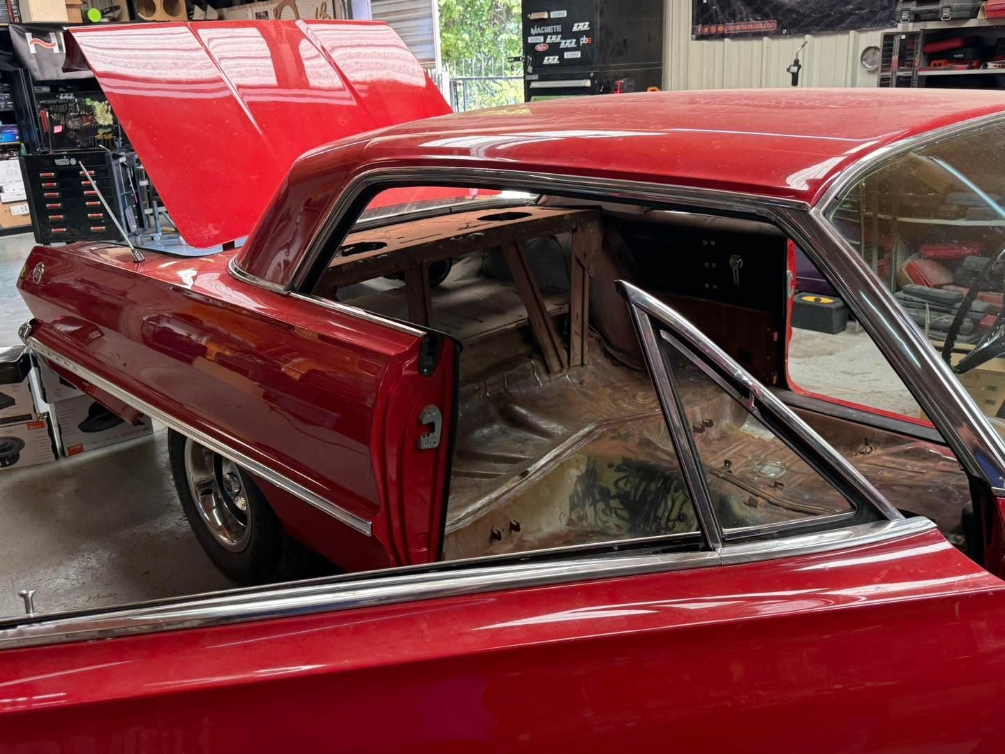Red classic car with open rear hatch and exposed roll cage in a garage workshop