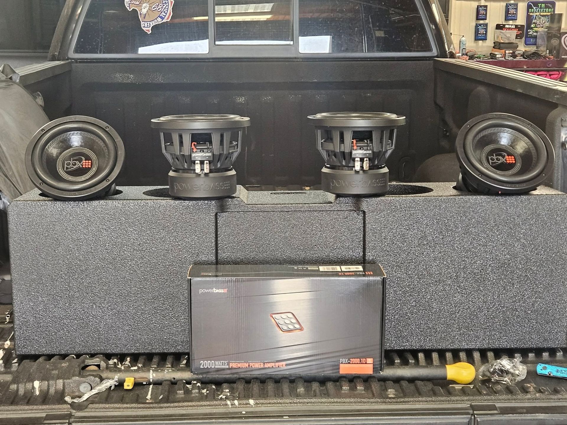 Car audio display with two speakers and a central amplifier on a gray carpeted shelf