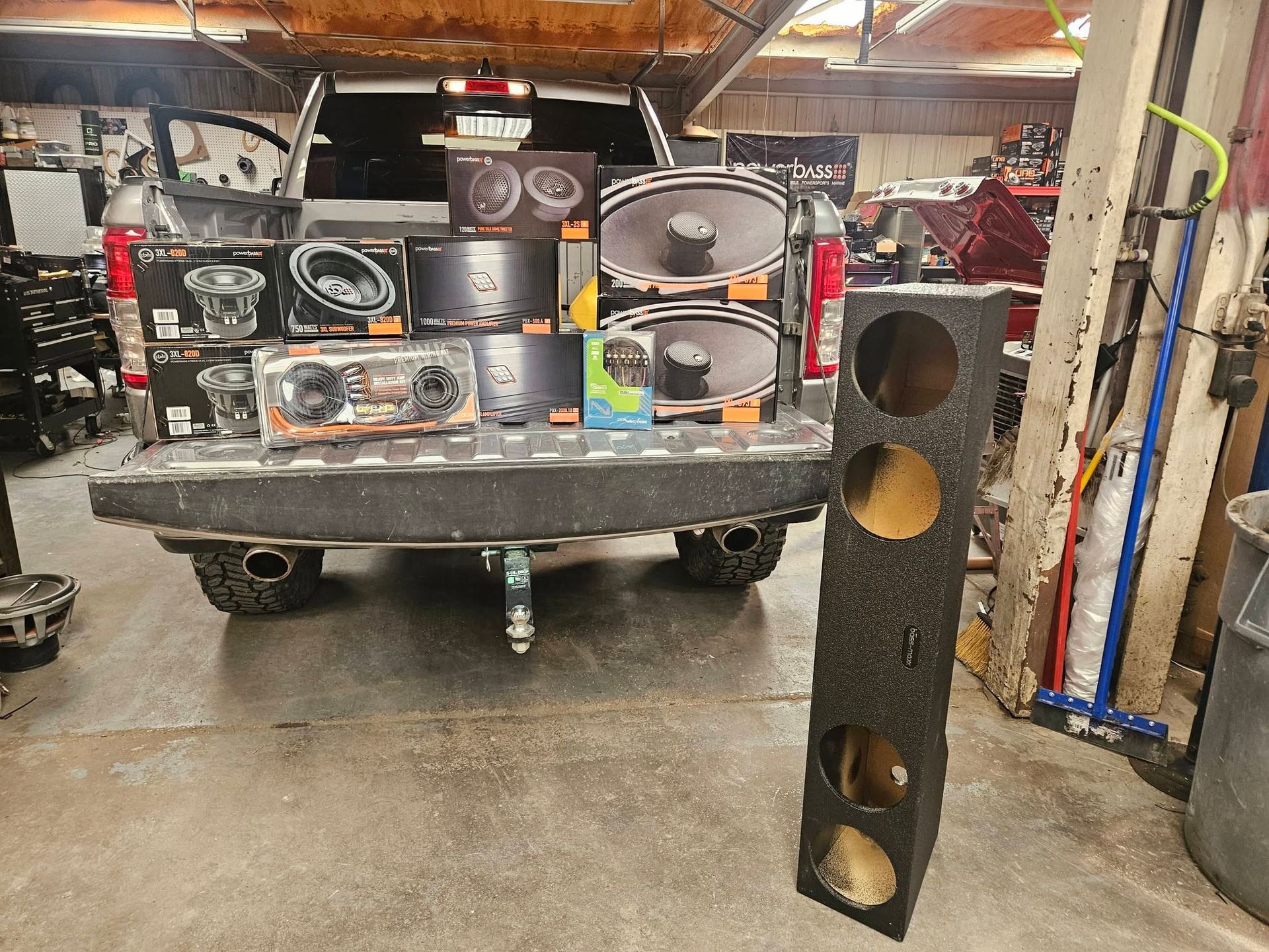 Speaker boxes and audio equipment arranged on a trailer in a garage, with a tall speaker cabinet in front.