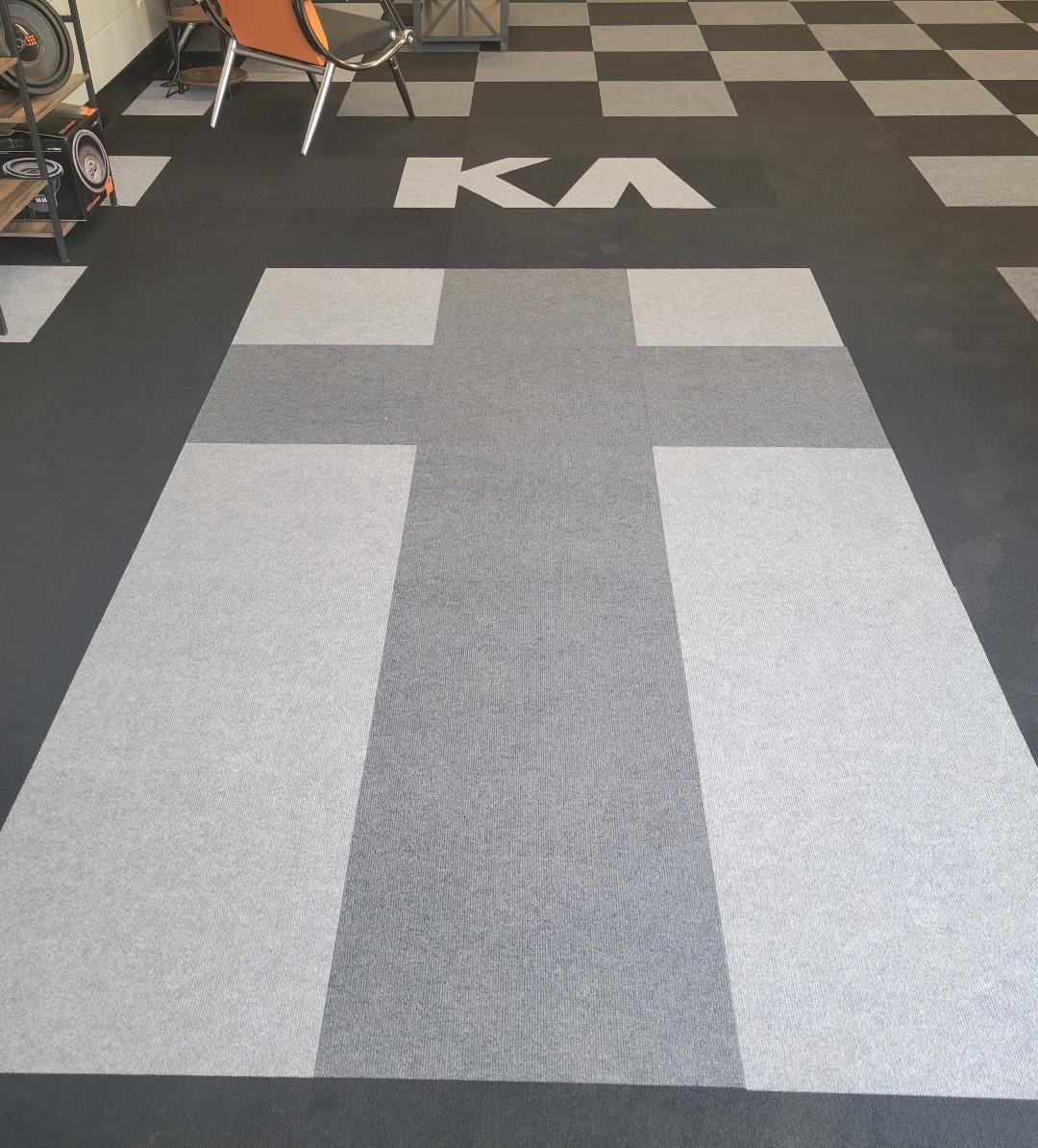 Gray carpet with a light square path in a gym or workshop, leading toward a checkered floor and chairs