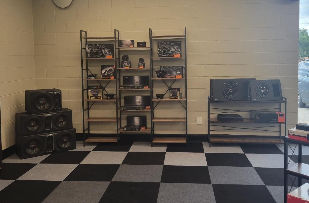 Empty room with black-and-white checkered floor, metal shelves, and stacked speakers along the walls