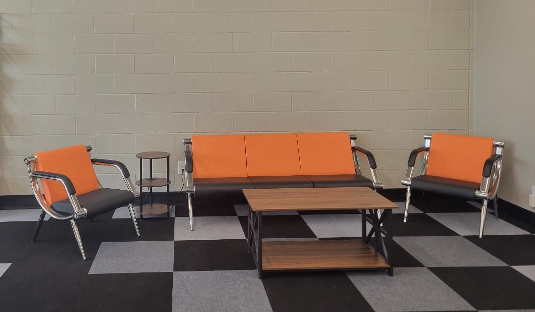 Orange and silver waiting room chairs around a wooden coffee table on a black-and-gray checkered floor