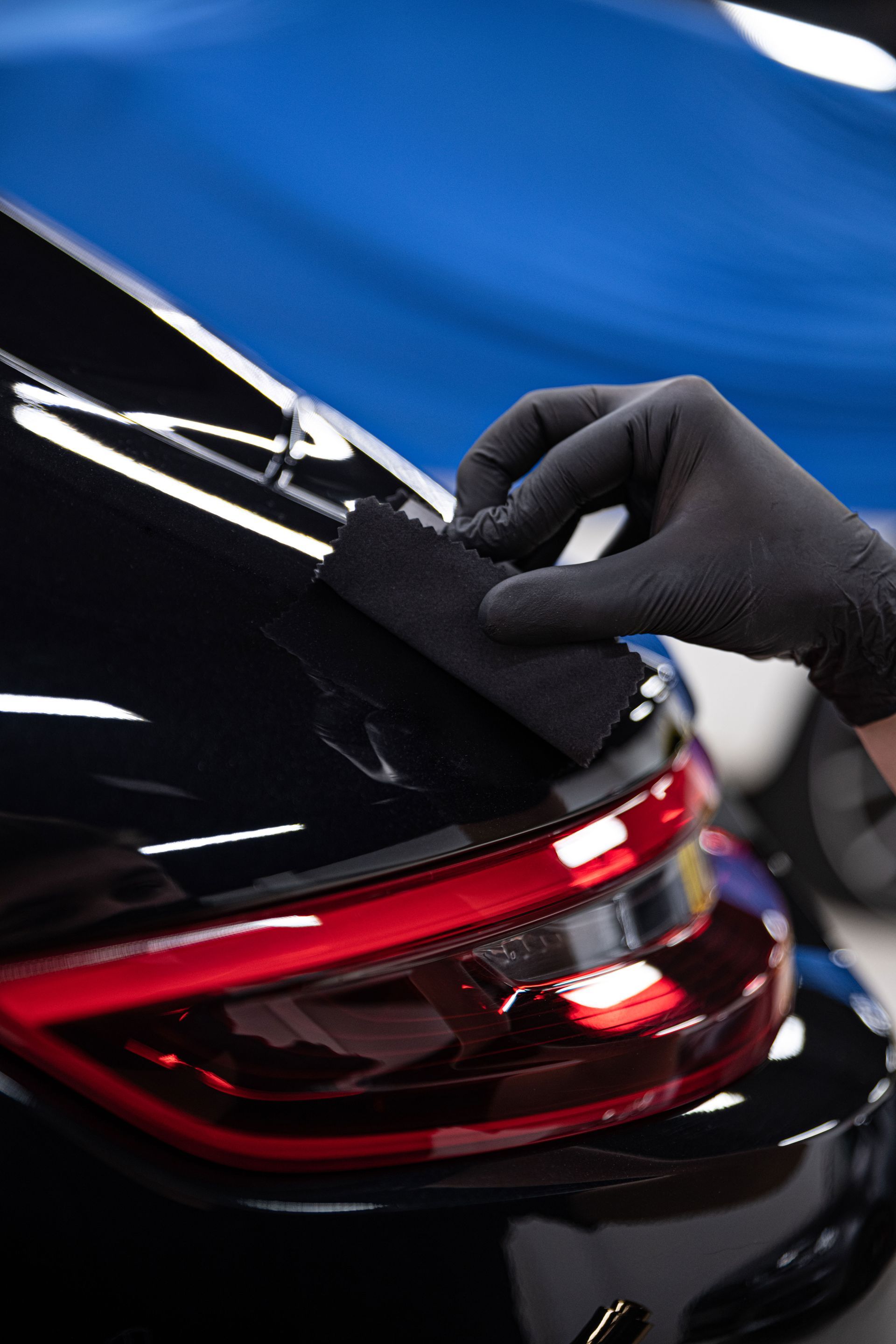 Person applying protective film to a black car headlight with a yellow squeegee. Indoors.