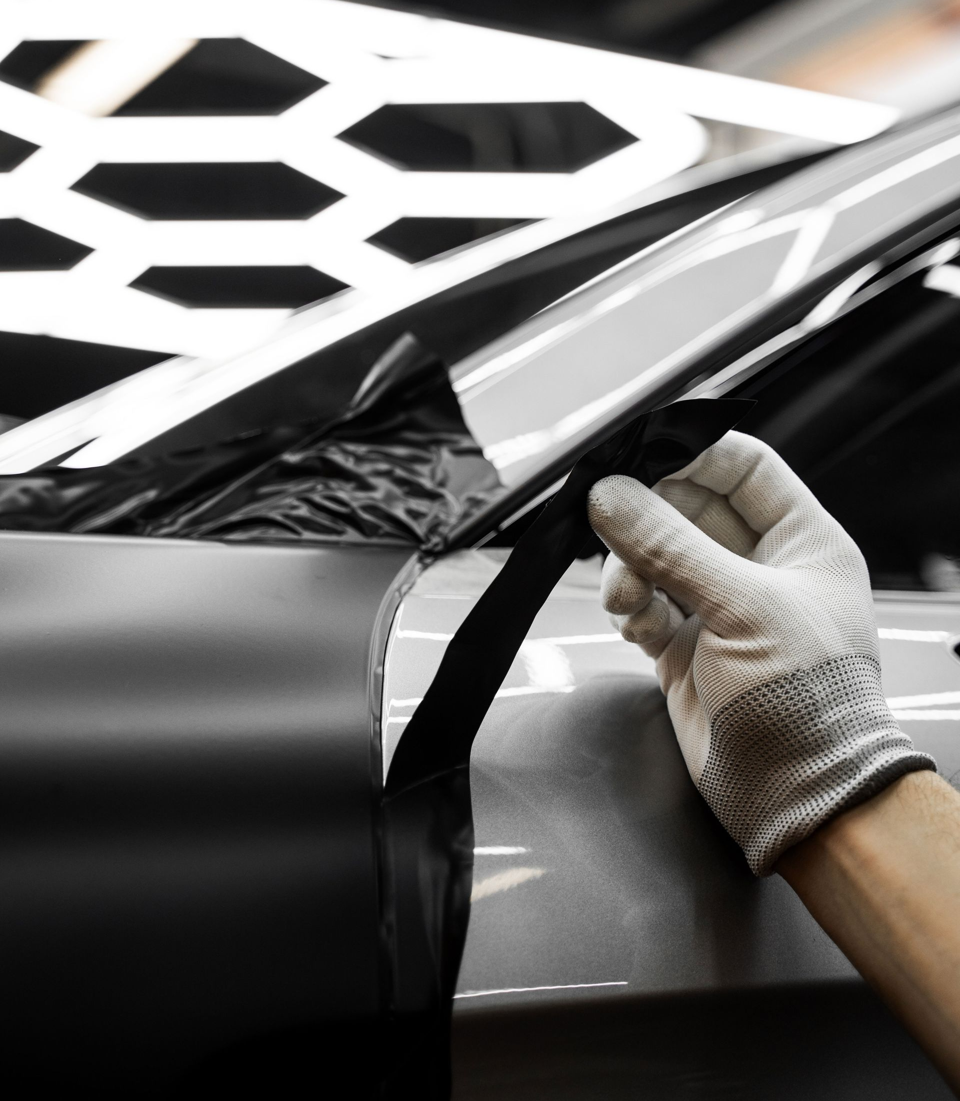 Person wearing black gloves smoothing a dark surface, likely in a workshop.