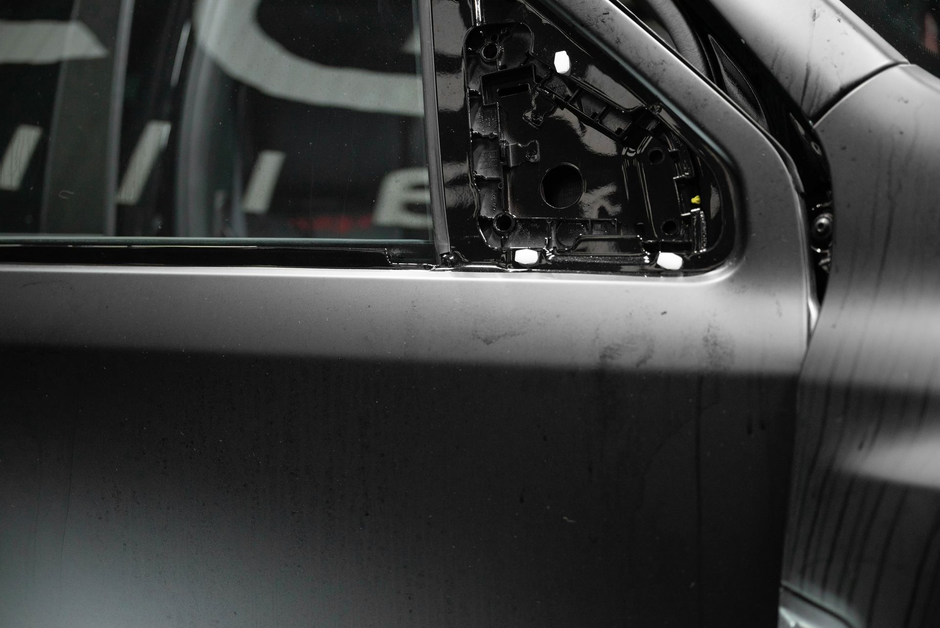 Close-up of a car door, revealing the frame for a missing side mirror. Dark, gray color.