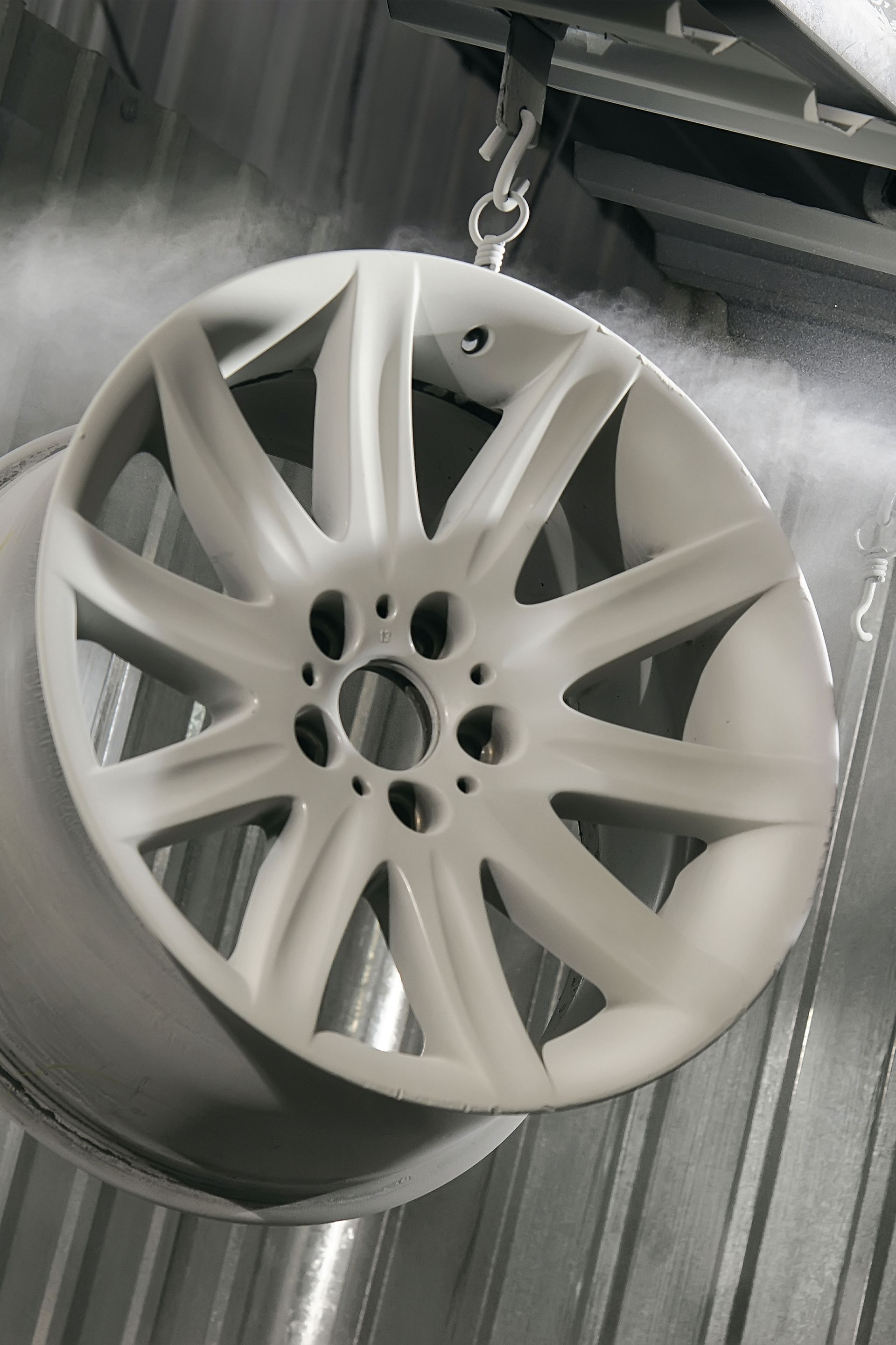 Wheel being powder coated, suspended in a spray booth.