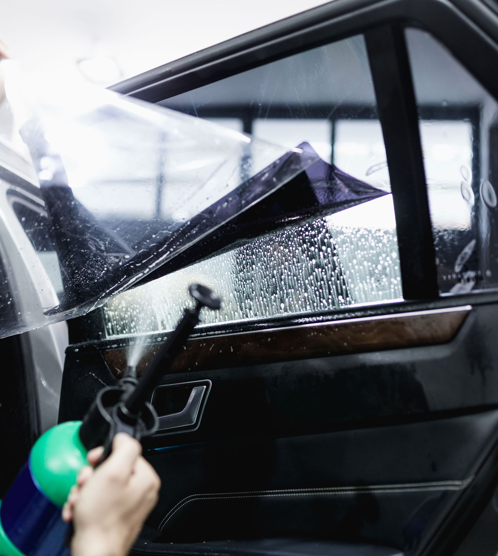 Gloved hand peeling black vinyl from a silver car panel, showing a car wrap installation.