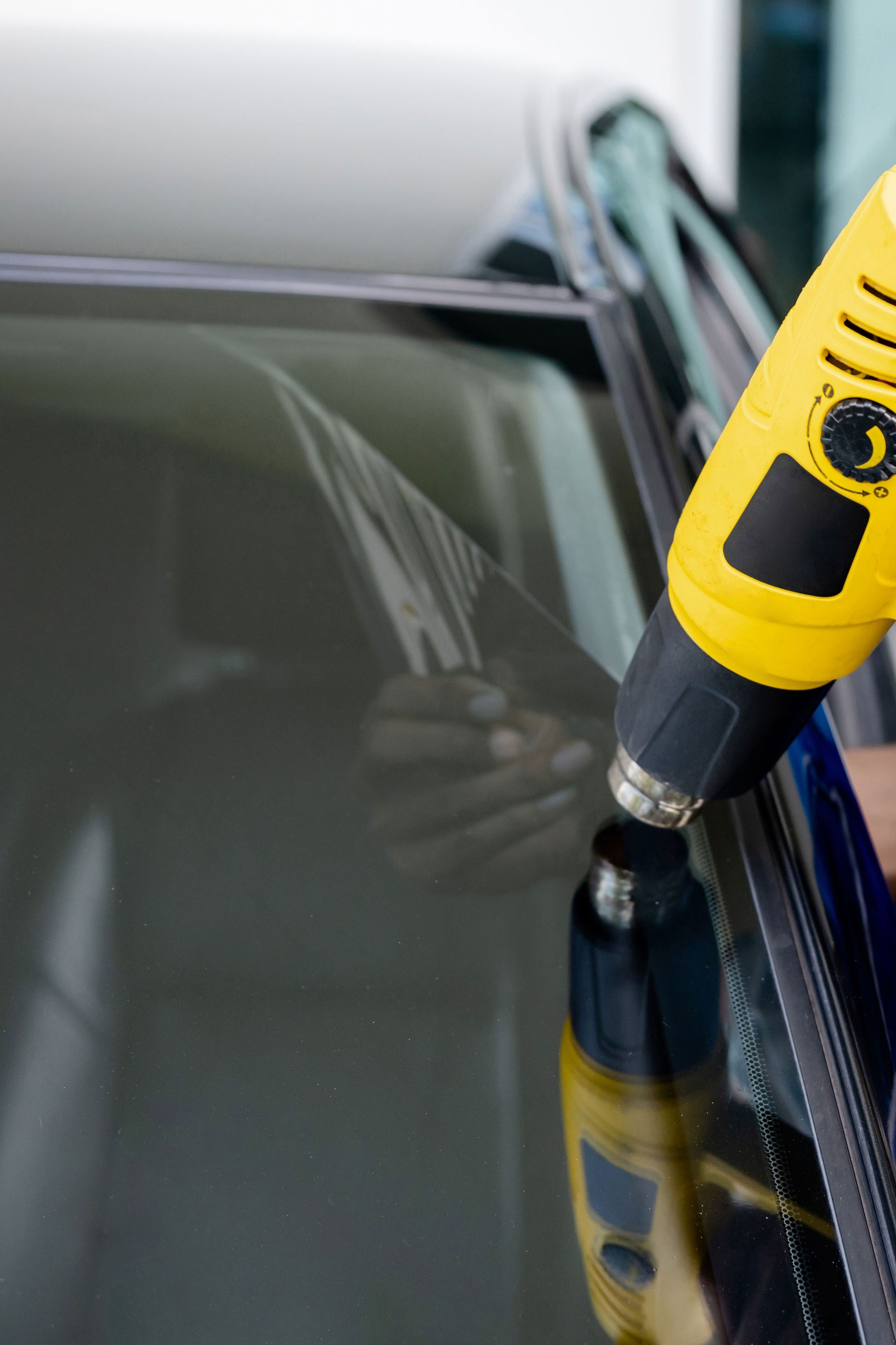 Applying window tint to a car window with a yellow heat gun; close-up shot.
