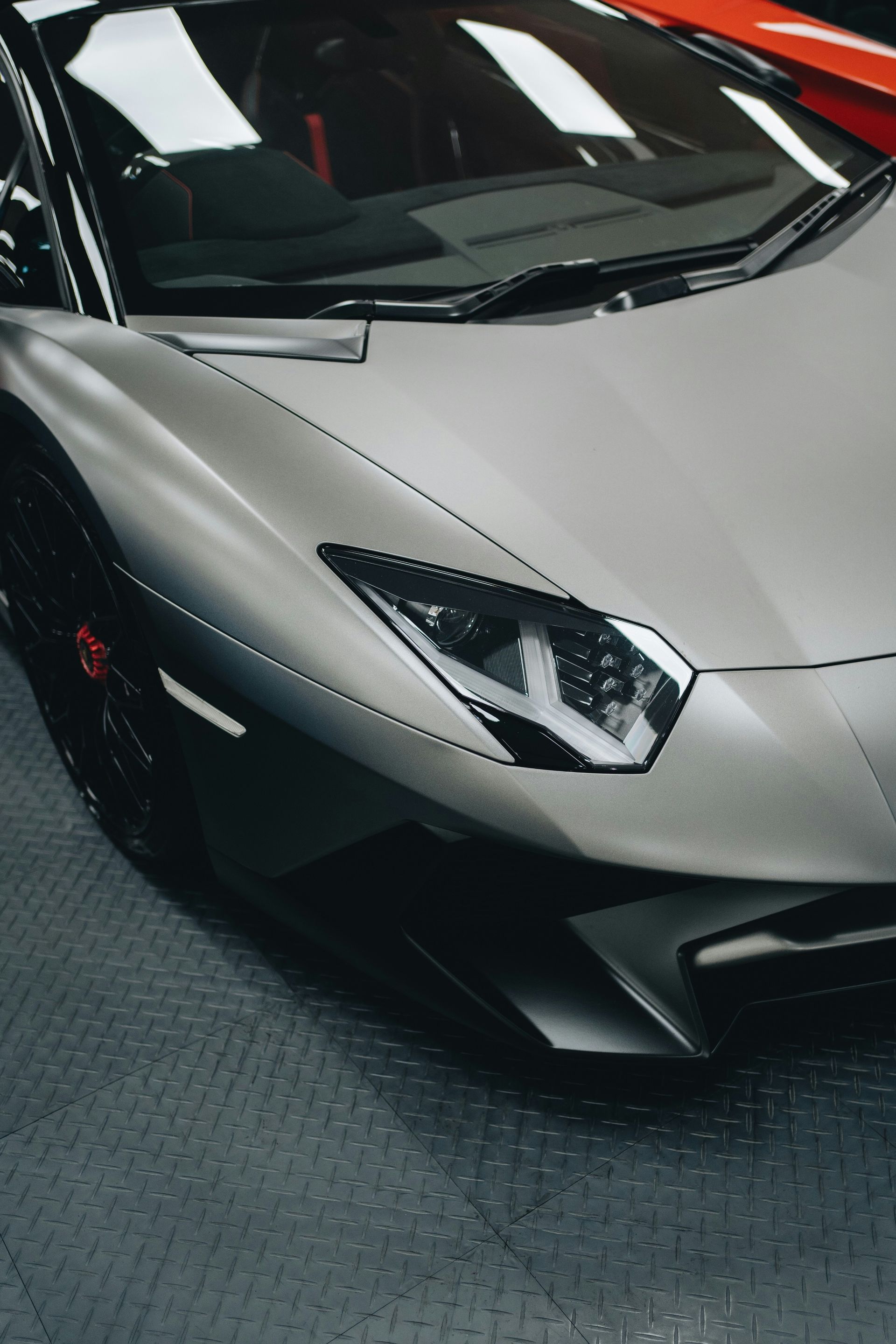 Silver Lamborghini sports car, headlights on, parked on a gray textured floor.