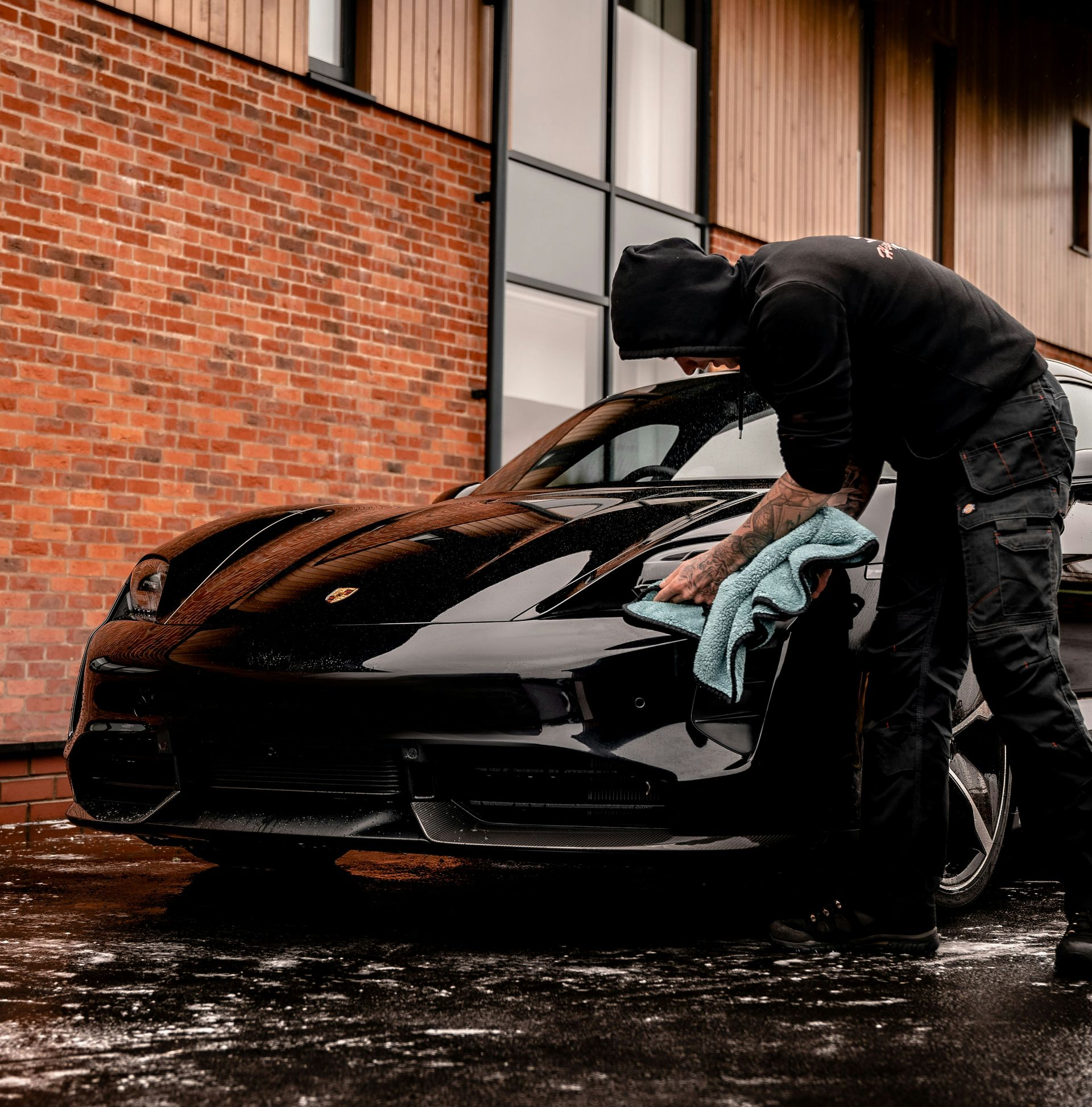 Man washing a black car. Brick building background, overcast day.