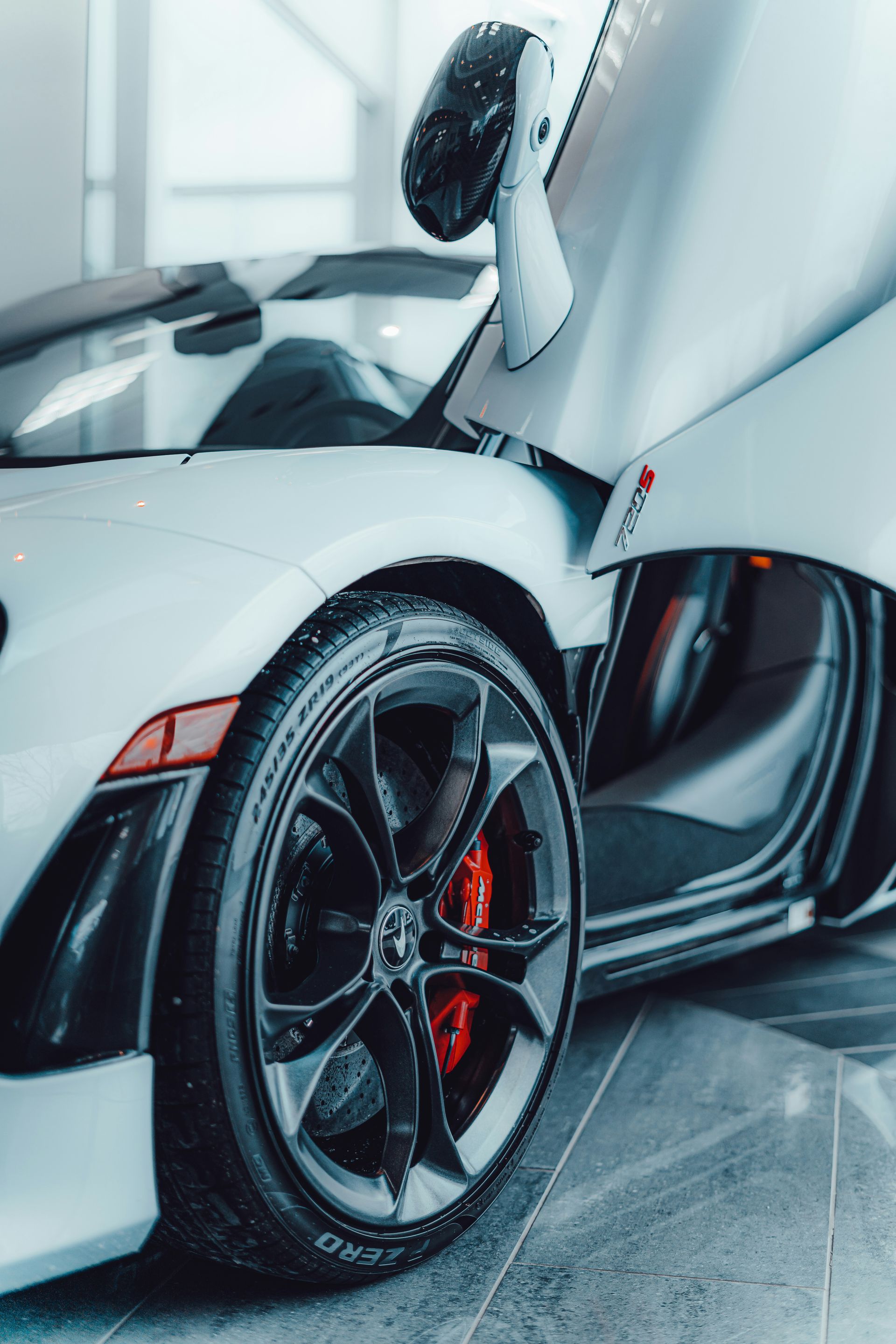 White sports car with open door, black rims, and red brake calipers.