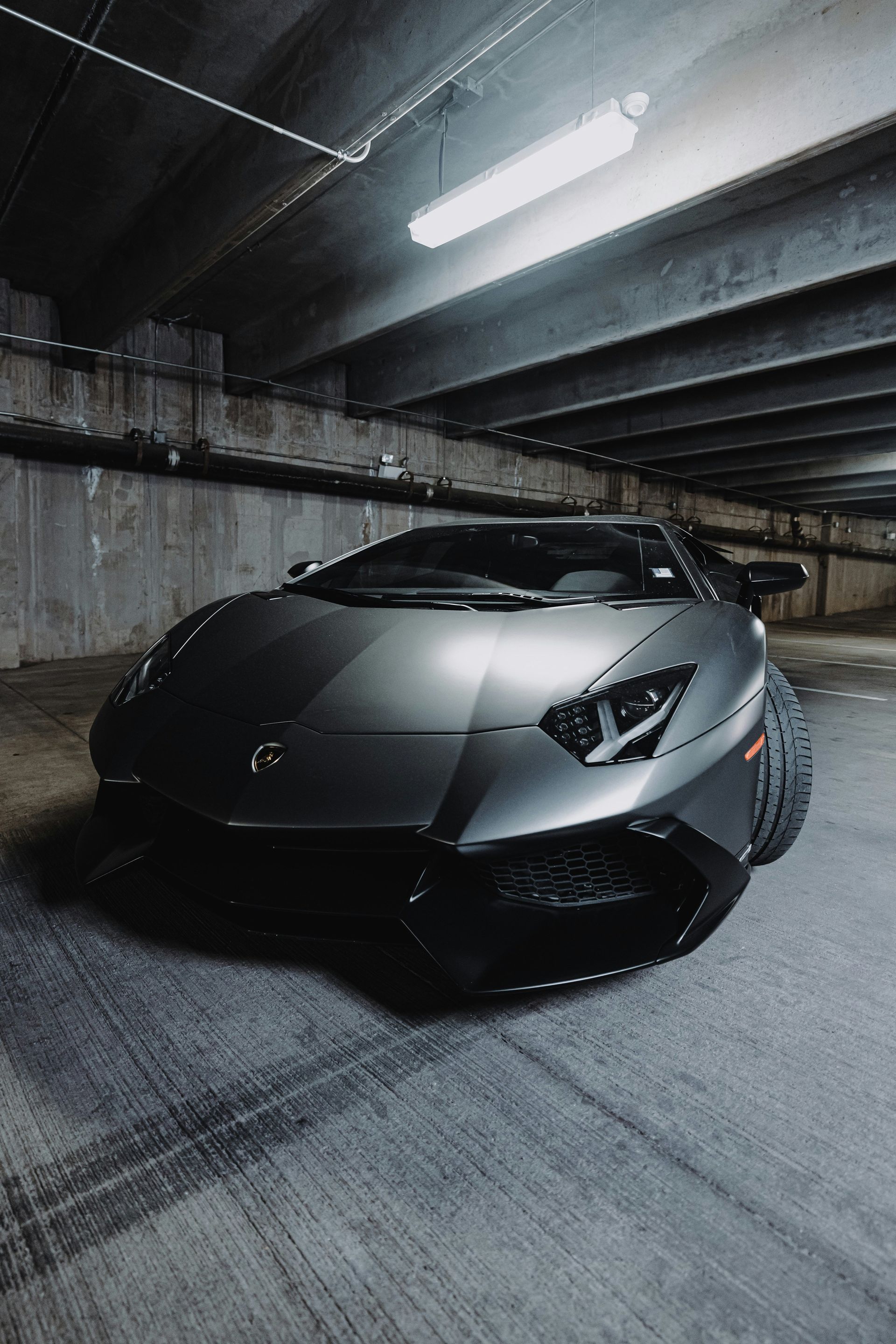 Gray Lamborghini Aventador parked in a dim, textured parking garage.