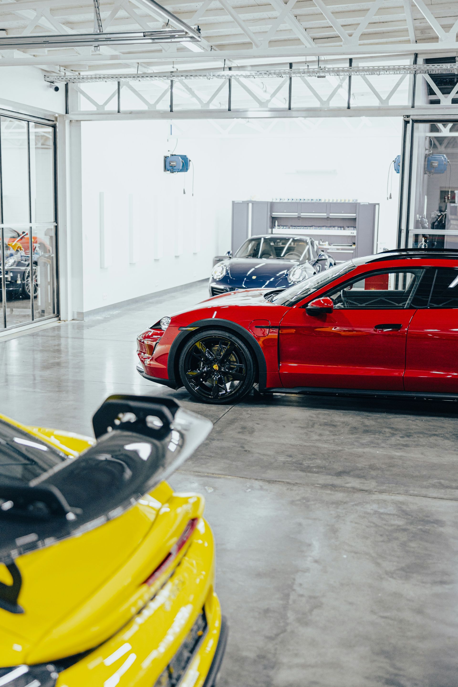 Red car in showroom with yellow car in foreground; other cars visible.