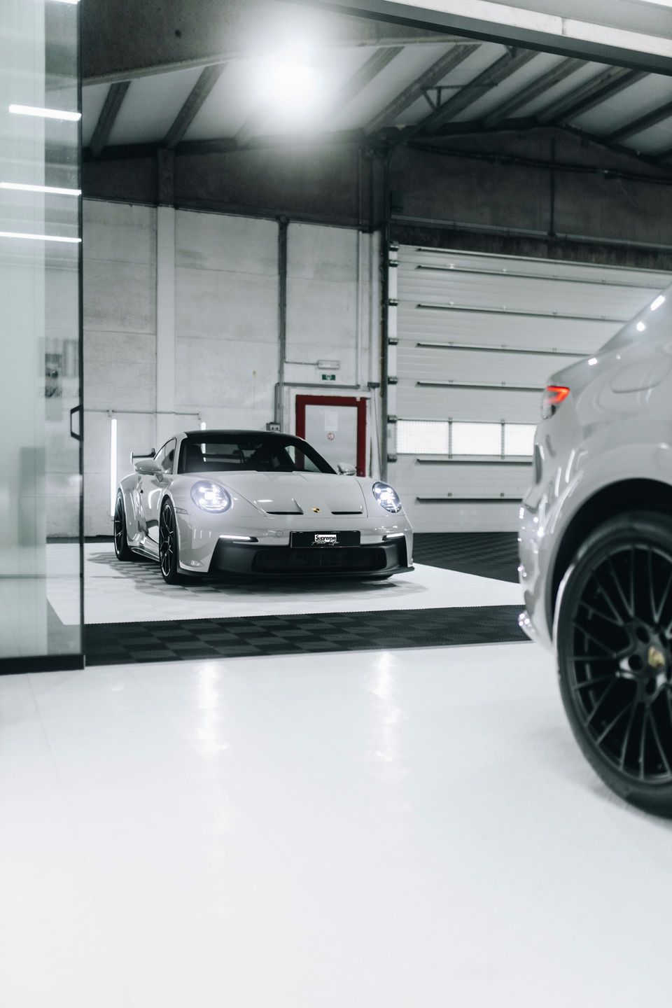 Silver sports car inside a garage, next to another car with a black wheel.