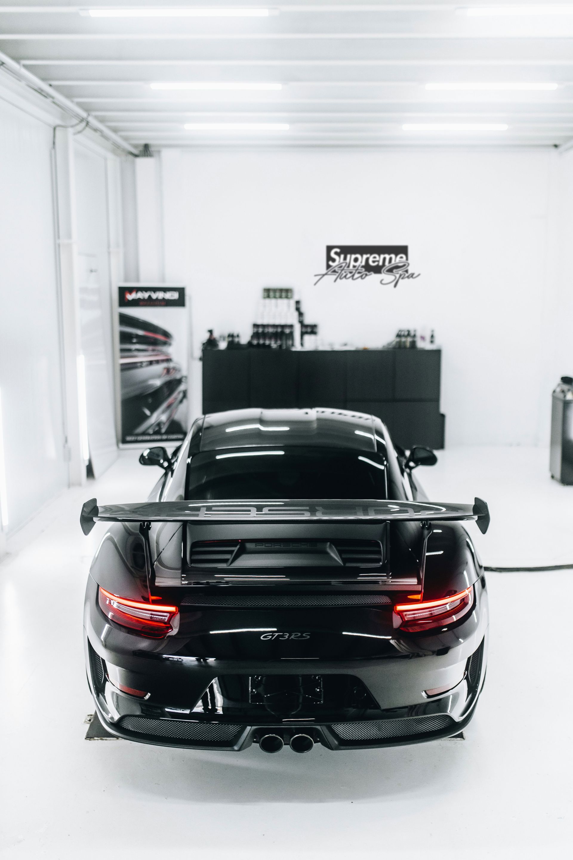 Black Porsche sports car in a bright white garage, rear view, large spoiler, professional detailing setting.