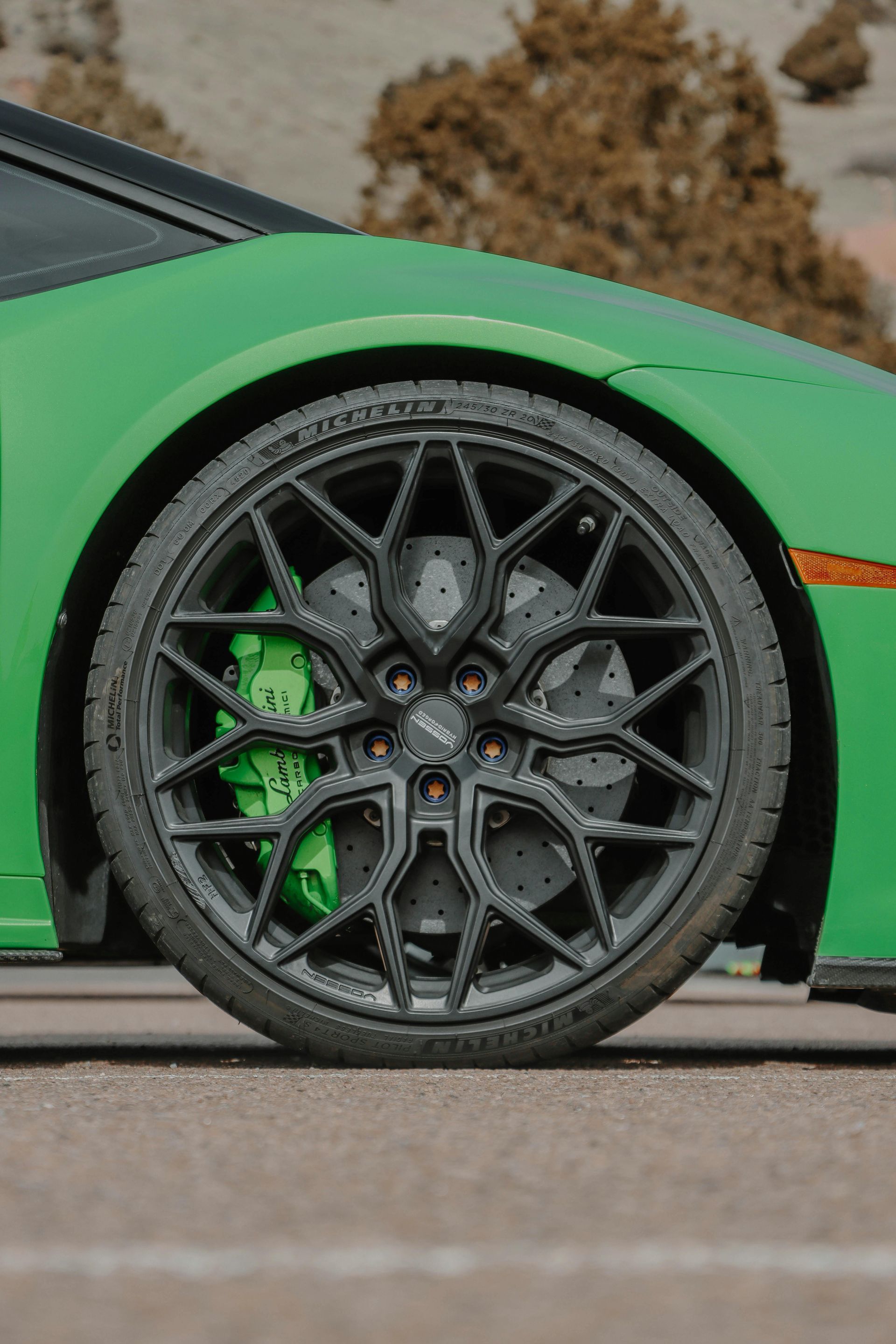 Green Lamborghini car's front wheel with black rim, tire, and bright green brake caliper on pavement.