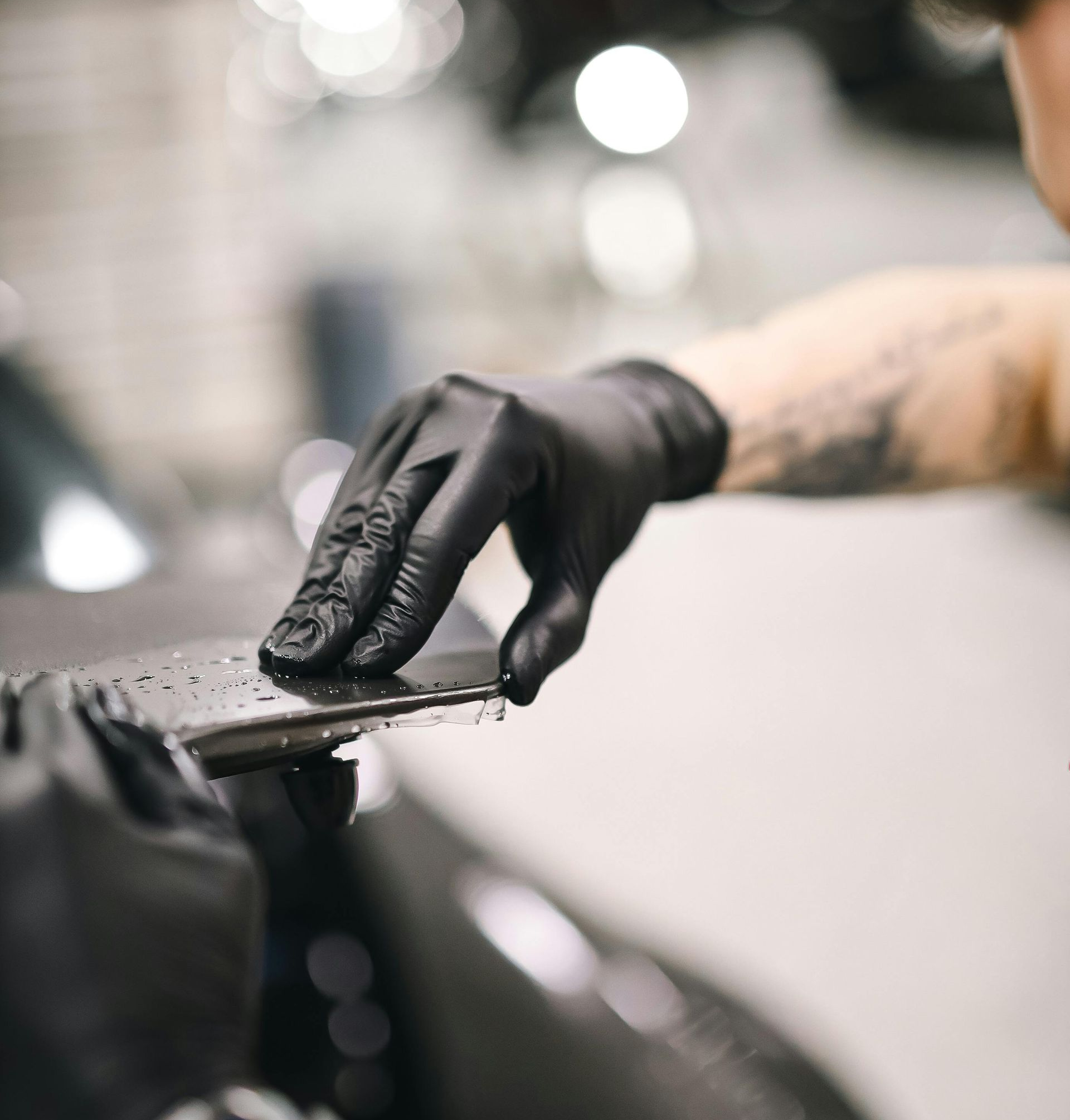 Person wearing black gloves smoothing a dark surface, likely in a workshop.