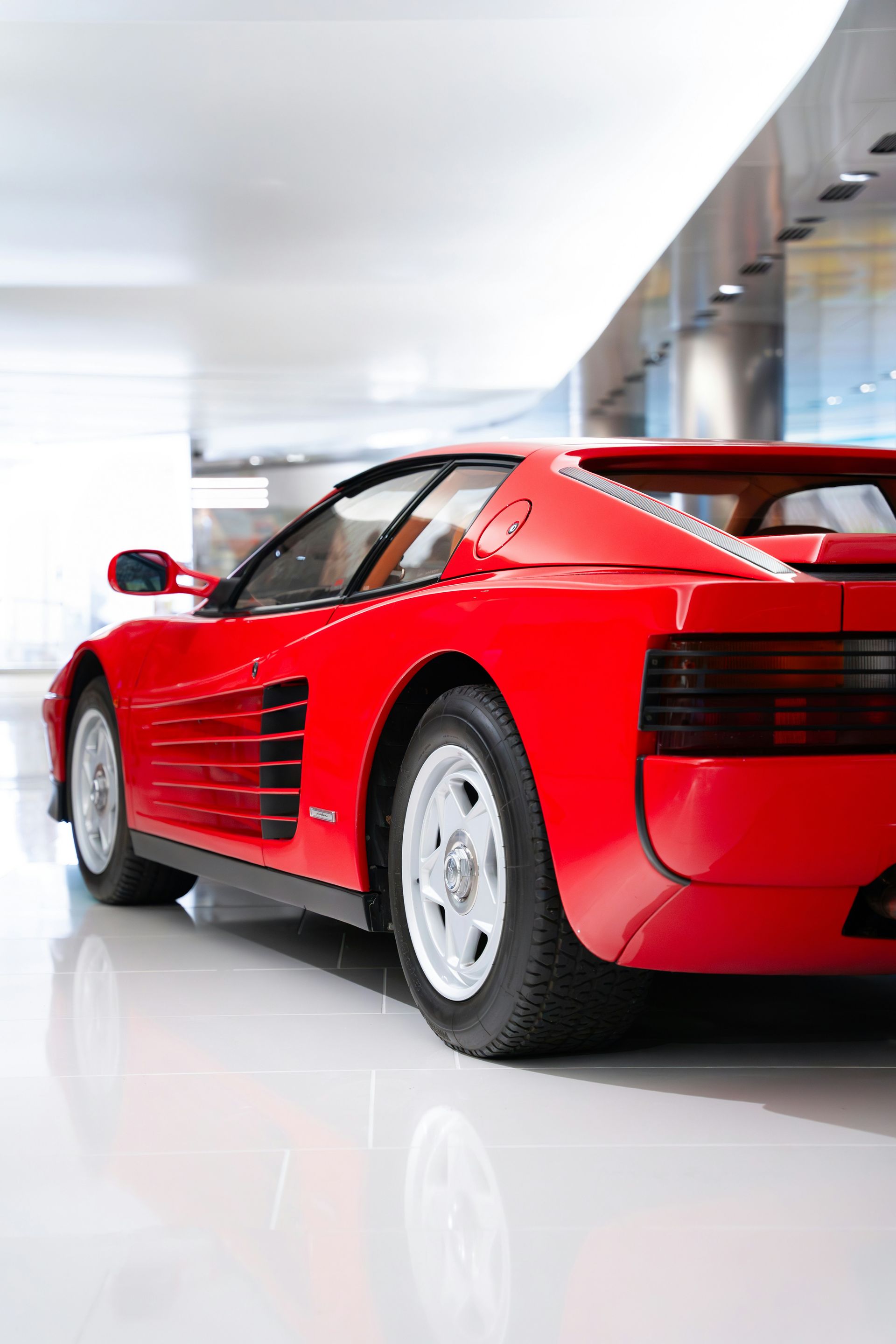 Red Ferrari Testarossa sports car parked indoors, white walls.