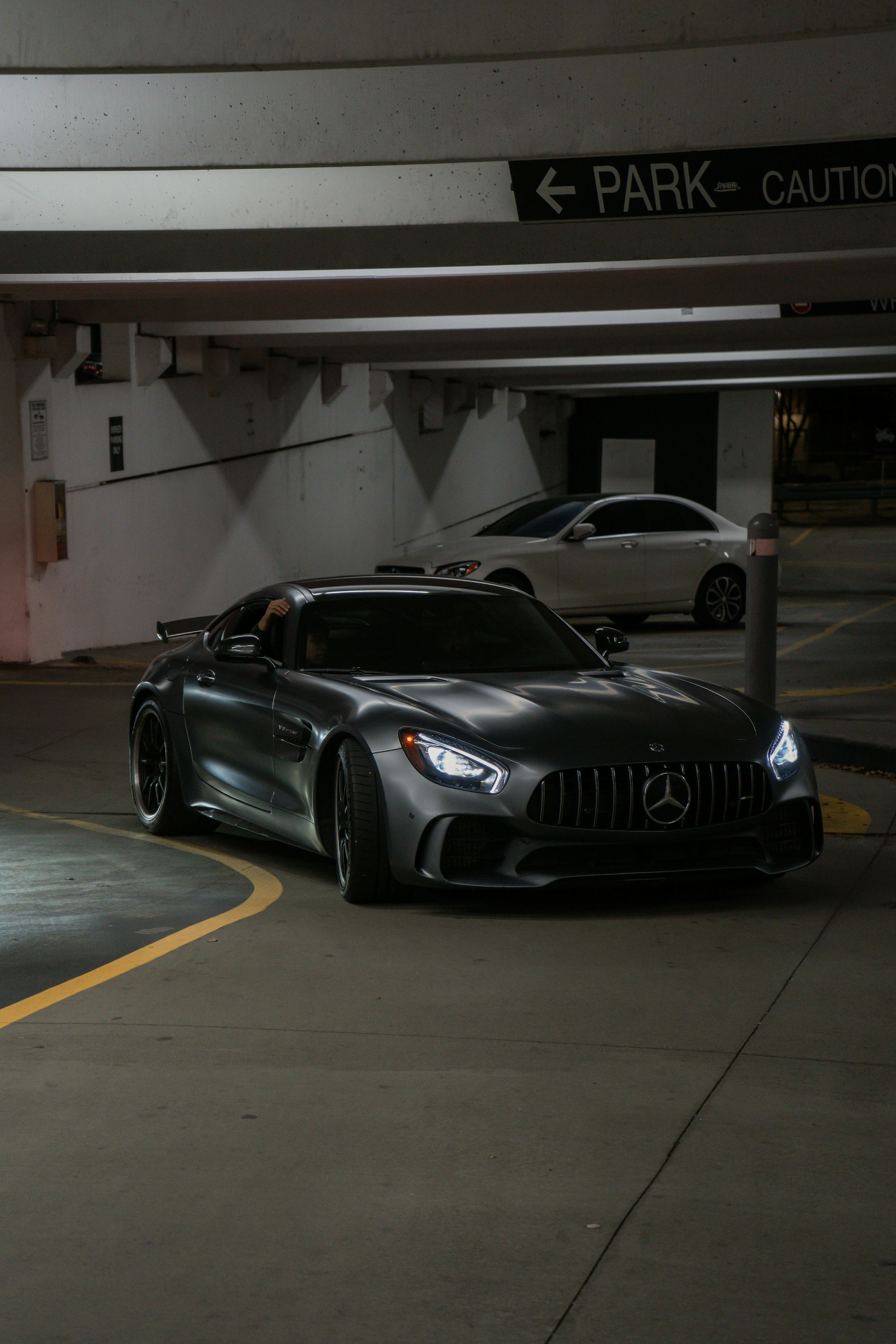 Dark gray Mercedes-AMG GT driving out of a parking garage, headlights on.