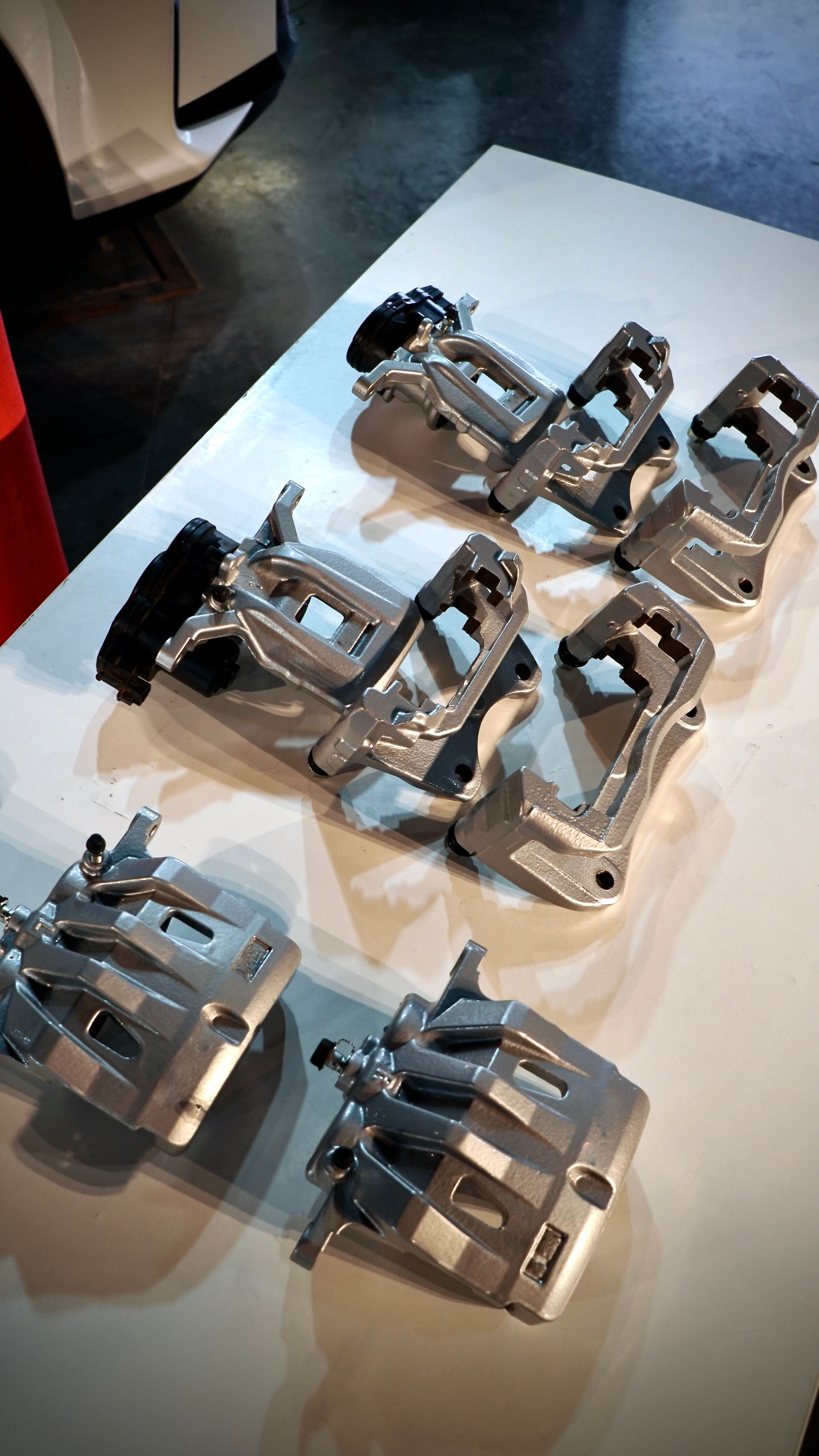 Silver-colored car brake calipers displayed on a white table.