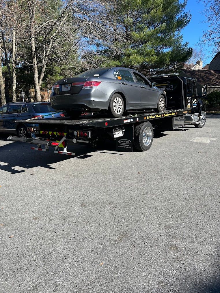 Gray sedan loaded on a flatbed tow truck on a roadside near trees under a clear sky | Village Repair