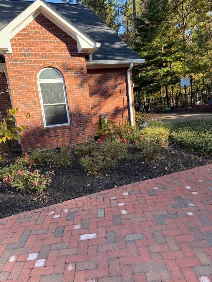 Brick house with arched window beside a red brick walkway and landscaped yard in sunlight