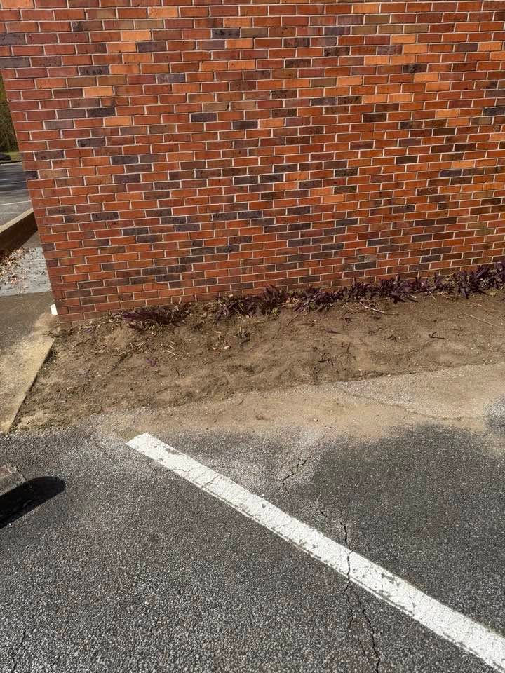 Brick building wall beside a parking lot with a white line and dirt strip at the base