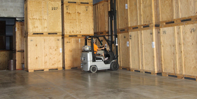 Forklift in a warehouse, moving among wooden crates.