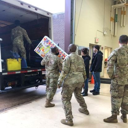 Soldiers unloading donations from a truck inside a building with onlookers.