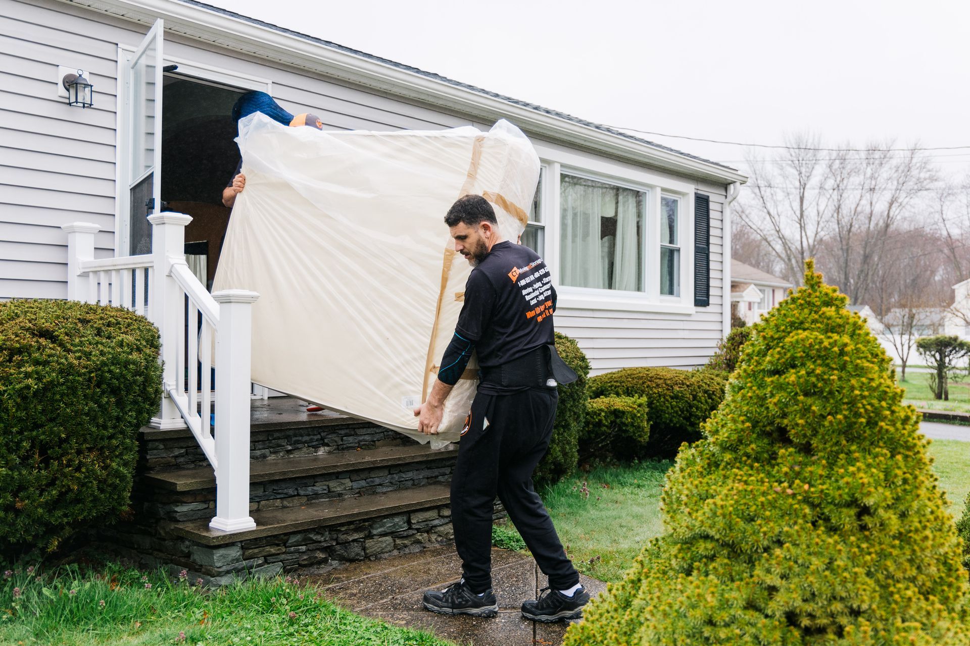 Two movers carrying a mattress out of a house's doorway.