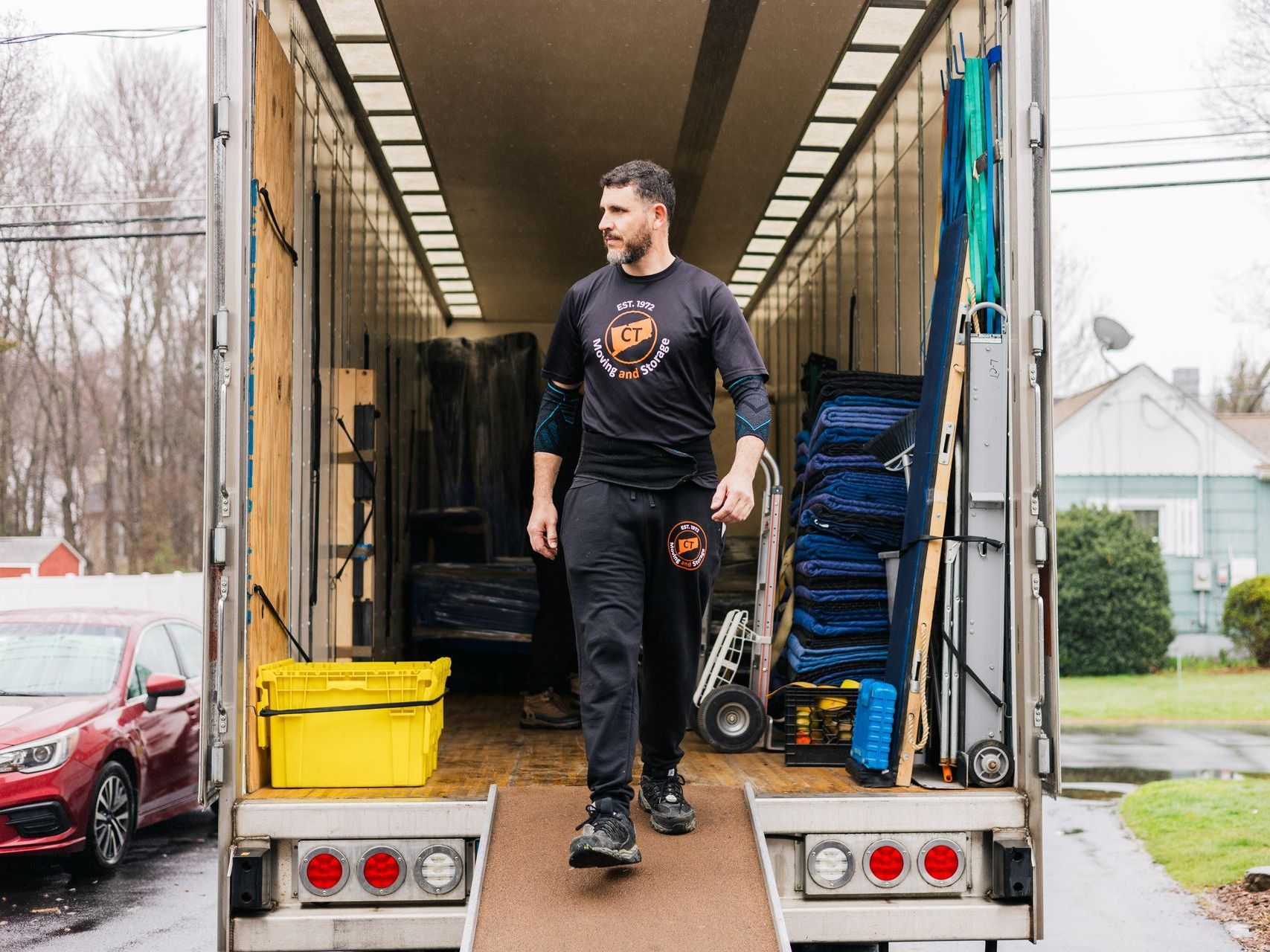 A person walks out of an open moving truck. The truck is filled with furniture and equipment.