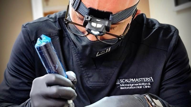 Person wearing headlamp and glasses, holding a blue tool, performing a procedure.