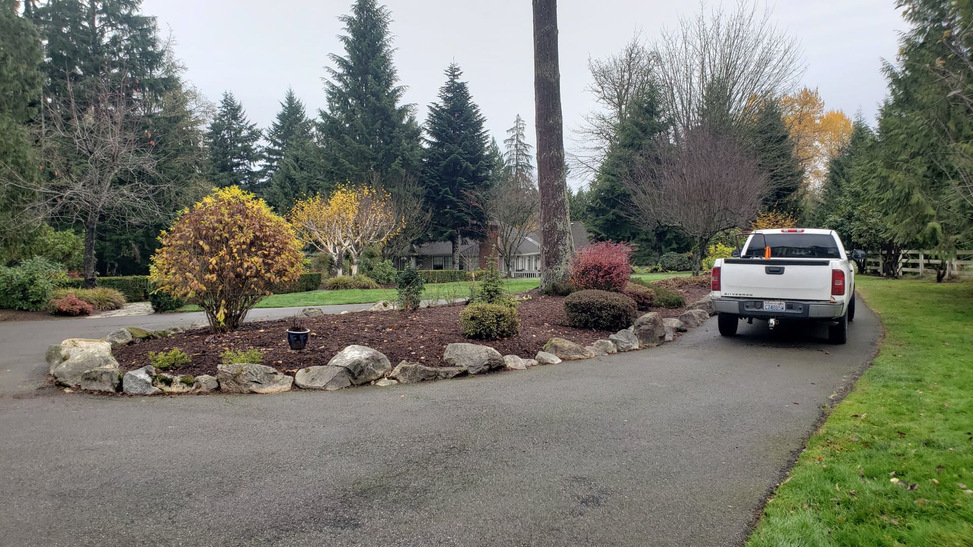 White pickup truck parked on a curved asphalt driveway, with colorful autumn landscaping and trees in the background.