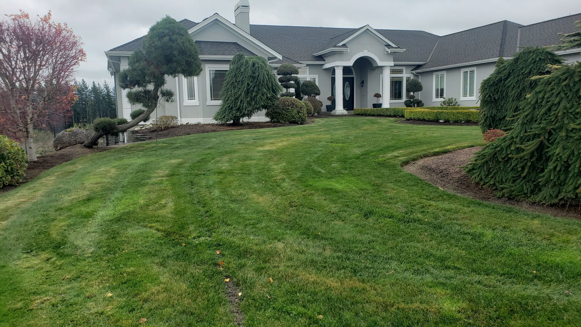 Large gray house with a well-manicured lawn and landscaping on an overcast day.