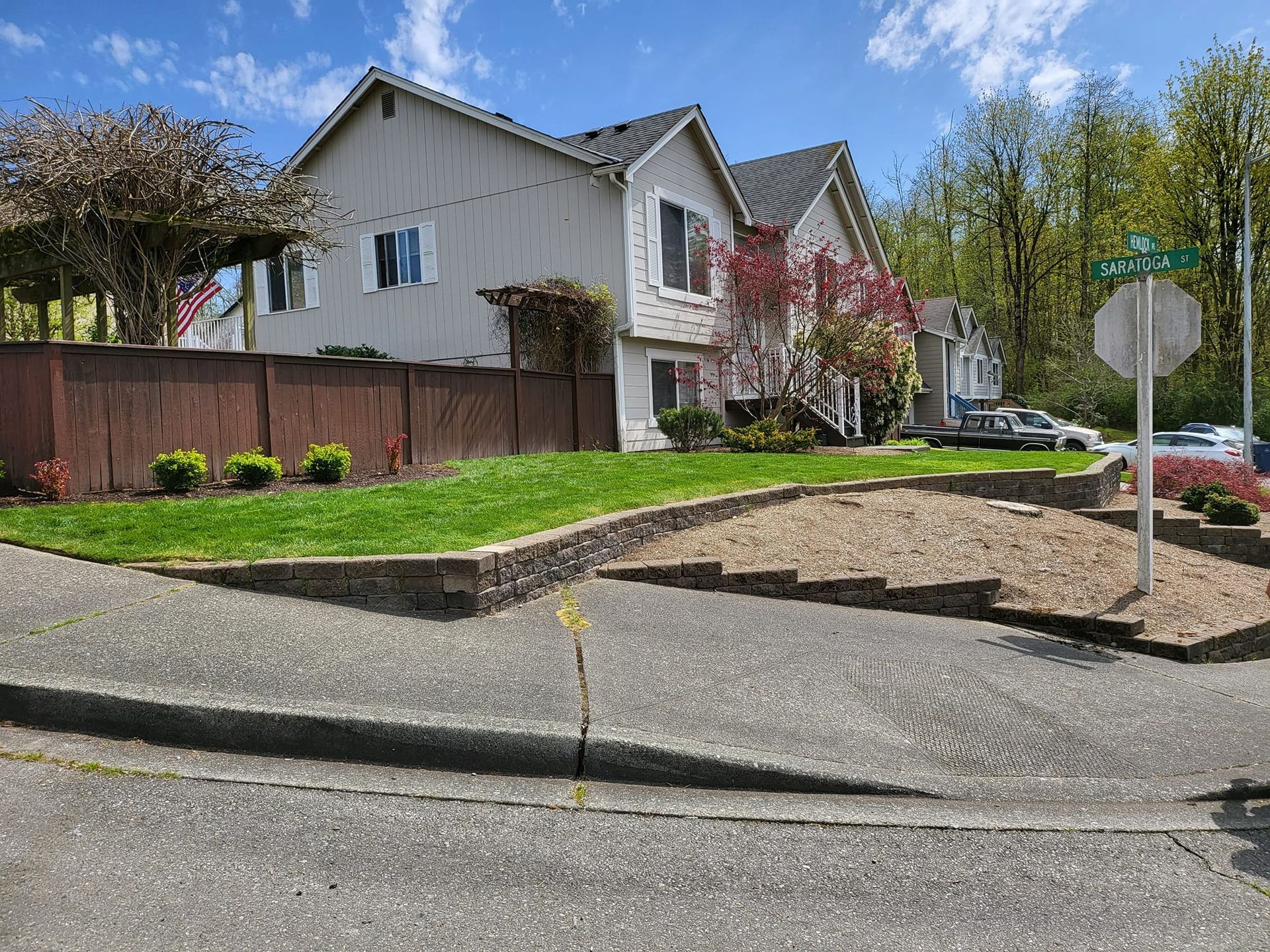 Two-story building with a brown fence and a grassy slope on a sunny day. A road sign is visible.