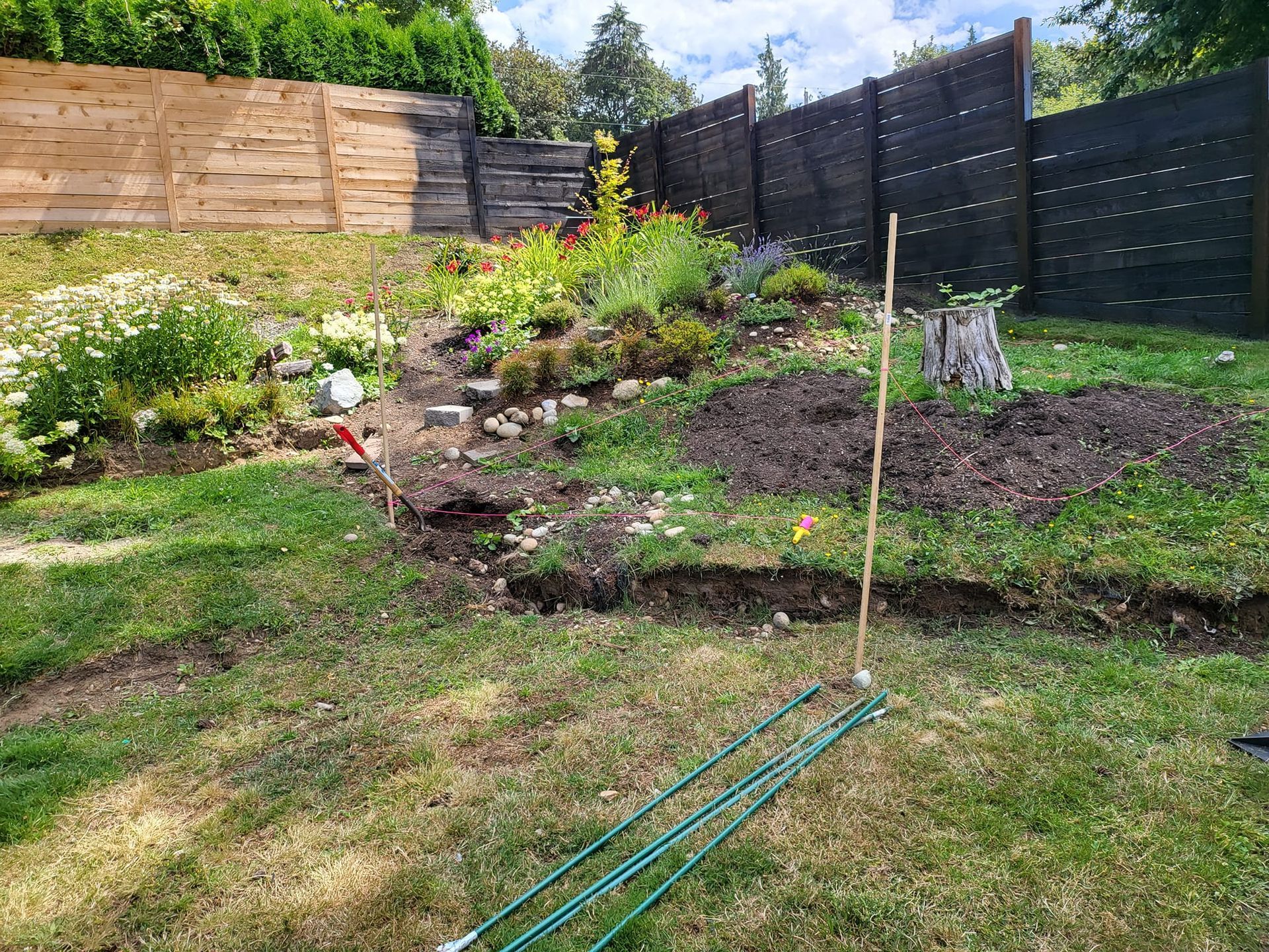 A sloped garden with grass in the foreground, tiered beds, and a dark wooden fence at the back.