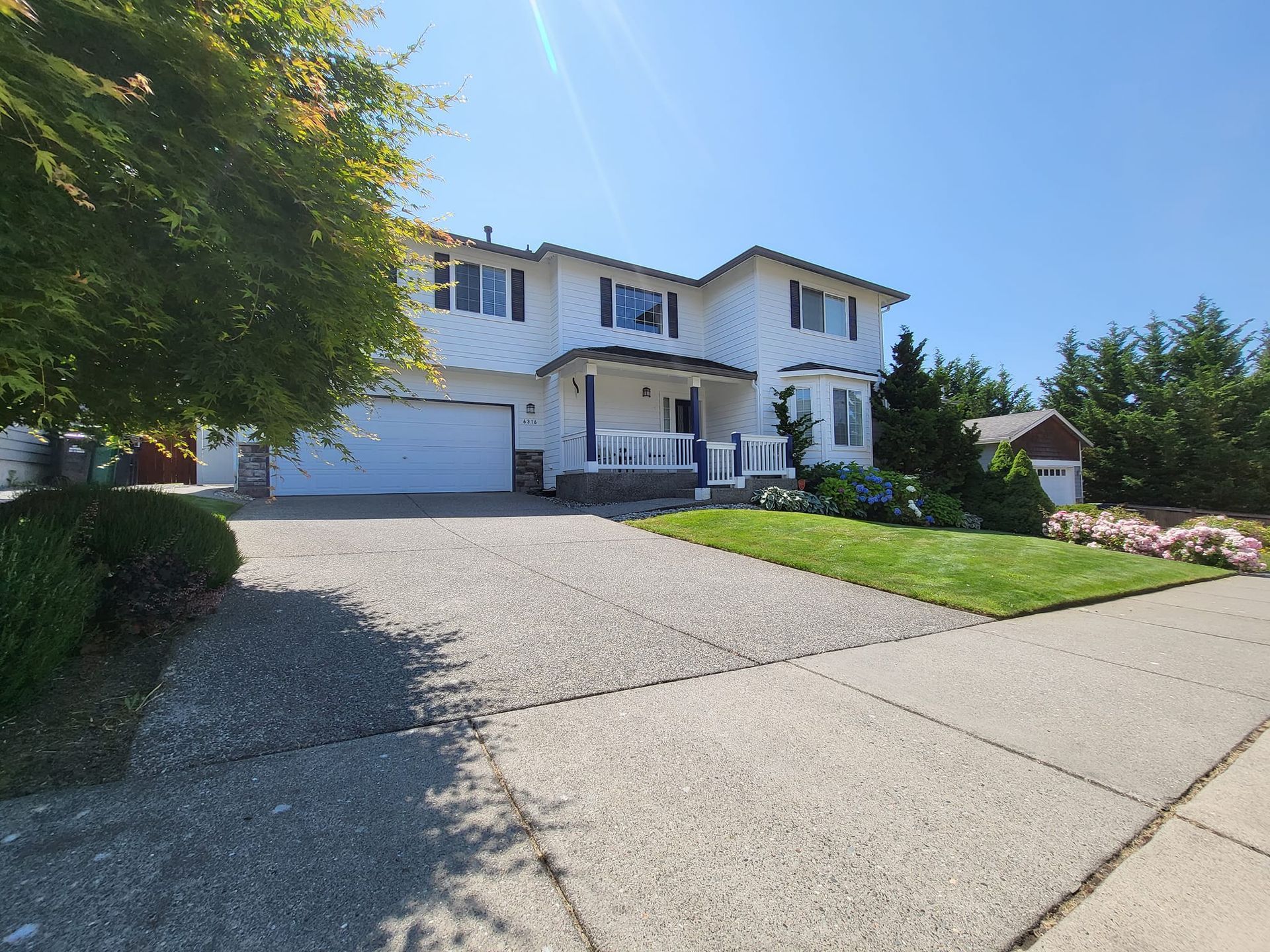 White two-story house with a driveway and small front lawn on a sunny day.