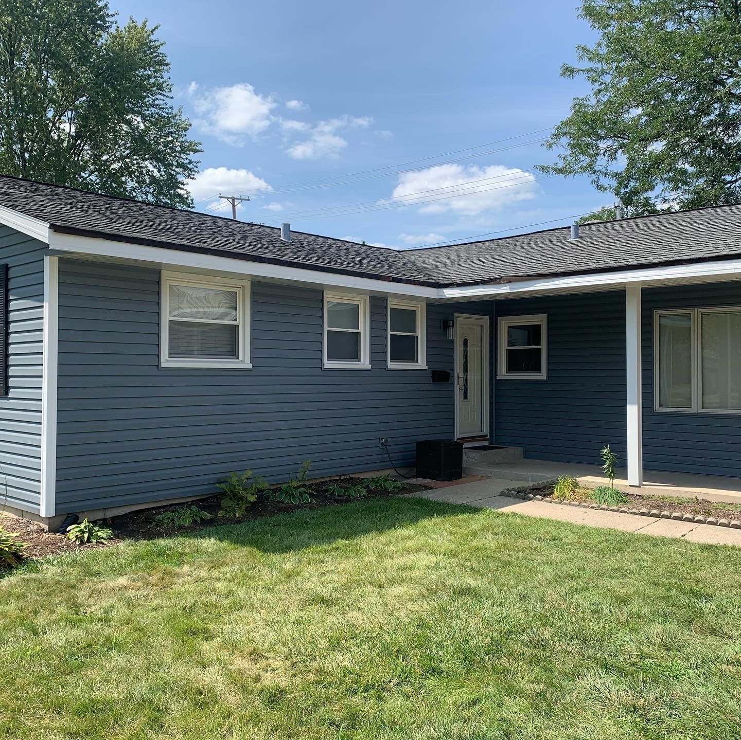 A blue house with a white porch and a gray roof is sitting on top of a lush green lawn.