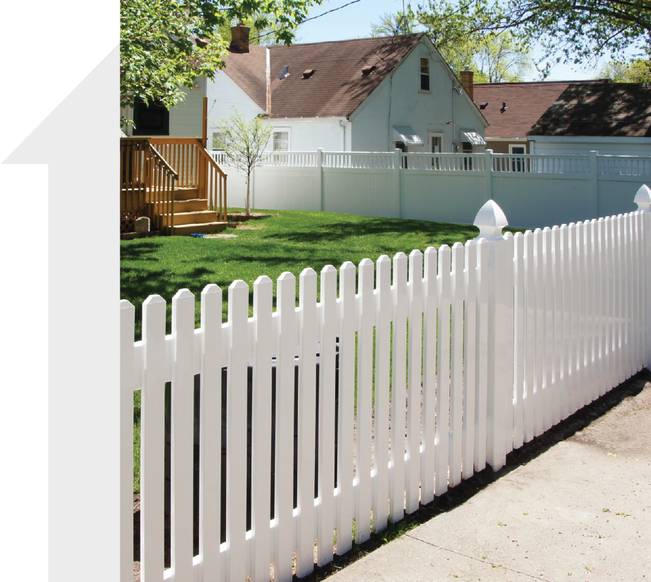 White picket fence along a driveway beside a green yard and suburban house on a sunny day