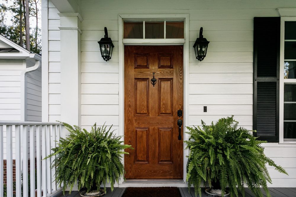 Wooden front door with black sconces, flanked by potted ferns on a white porch.