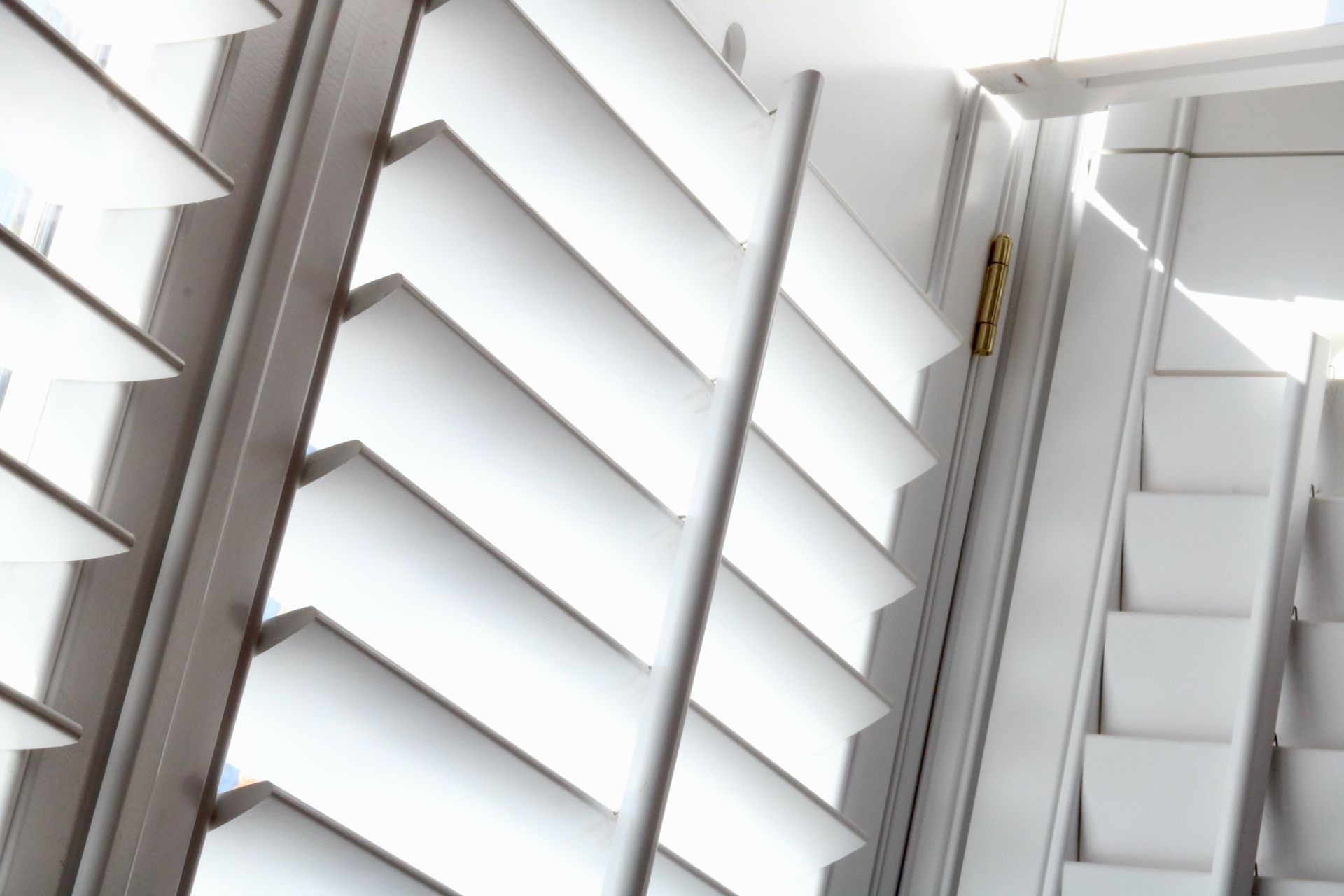 Close-up view of white plantation shutters with horizontal slats partially open, allowing light to filter through.