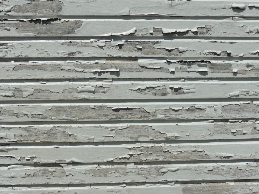 Cracked/peeling siding on a house that needs to be replaced.