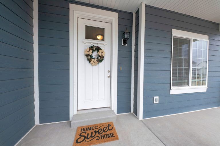 A blue house with a white door and a welcome mat that says home sweet home