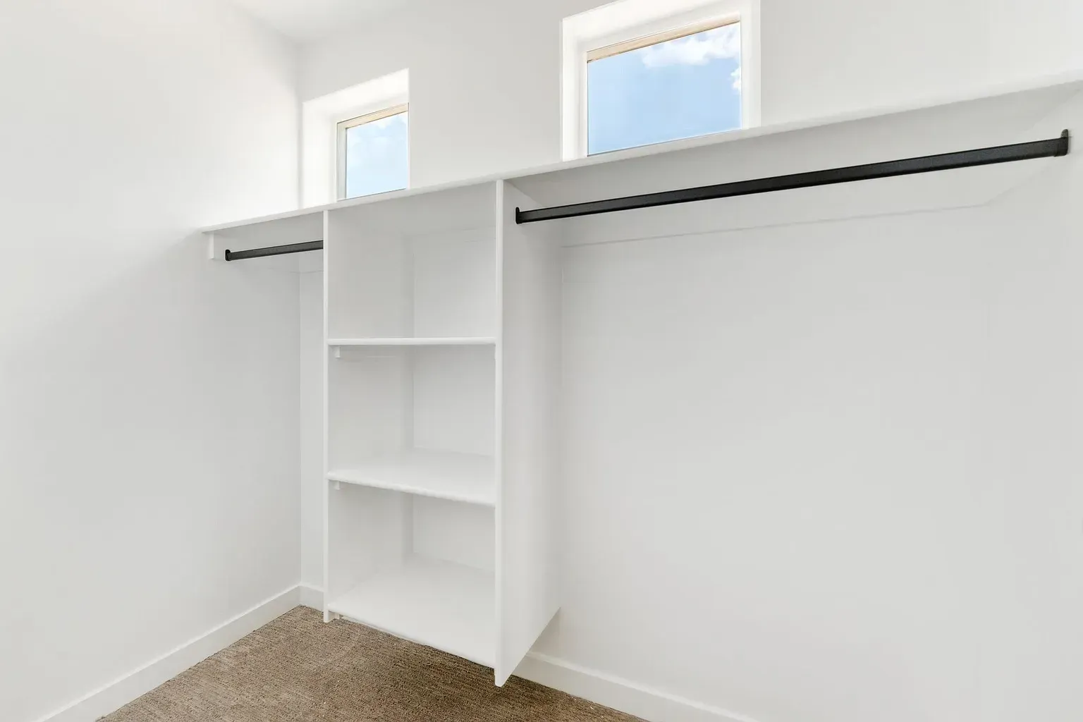 Bright white walk-in closet with built-in shelving and two hanging rods, window above.